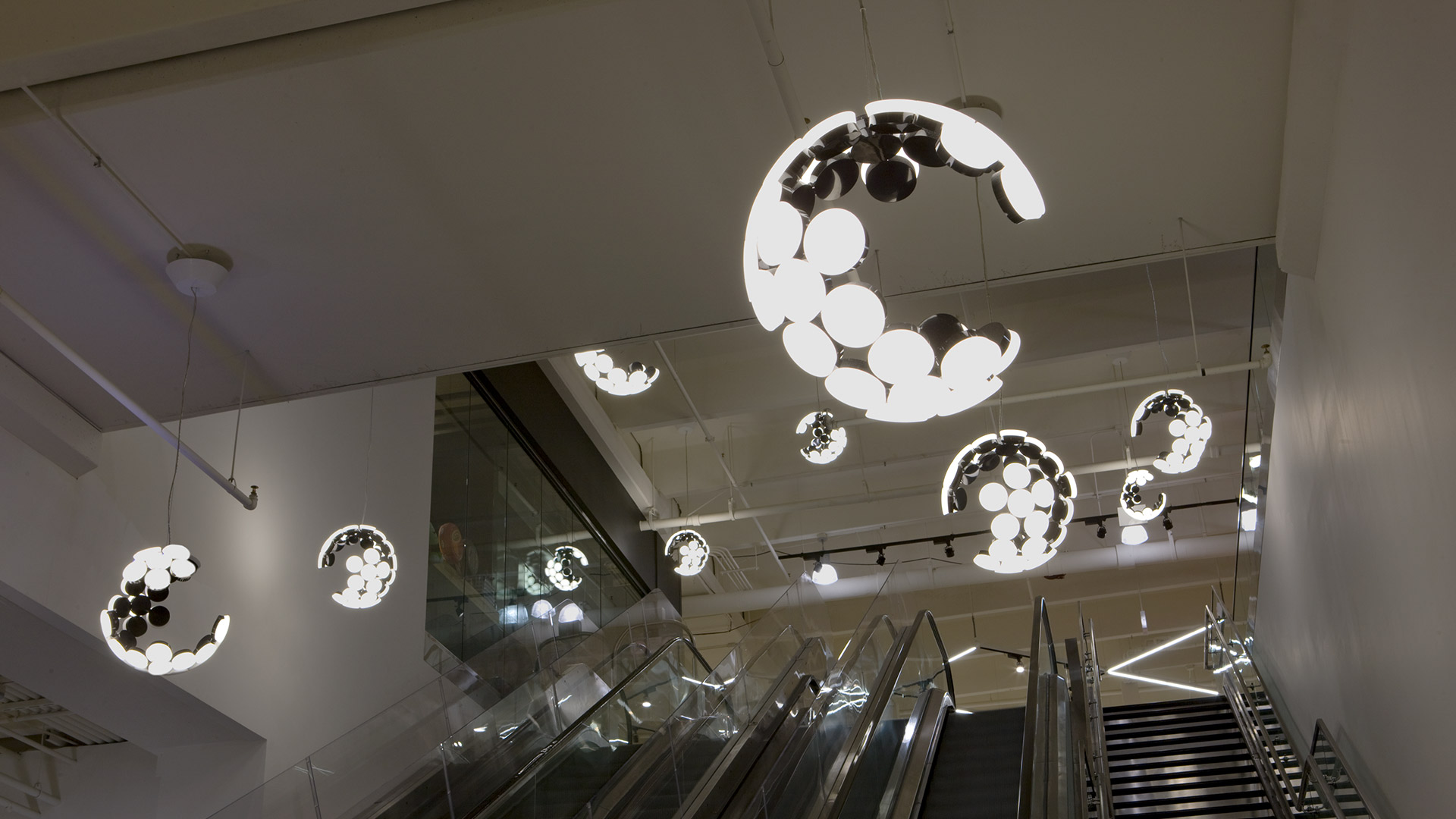 Two Artemide Scopas pendant lamps in black and white, featuring crescent-shaped frames with overlapping disc diffusers on dark cords