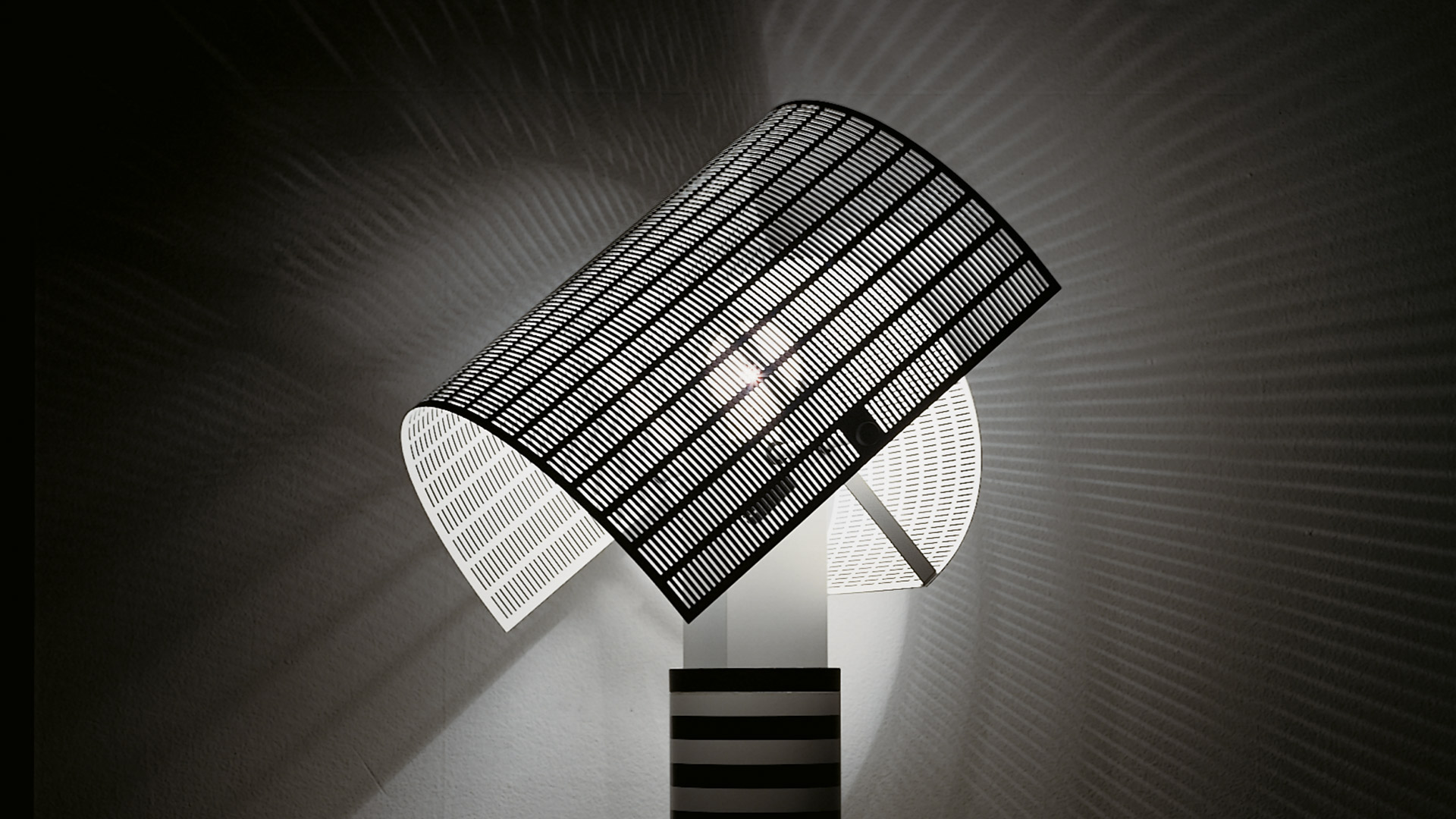 Soggiorno moderno con lampada da tavolo Artemide Shogun sulla scrivania, base a righe e diffusore bianco, accanto a un mobile TV a parete