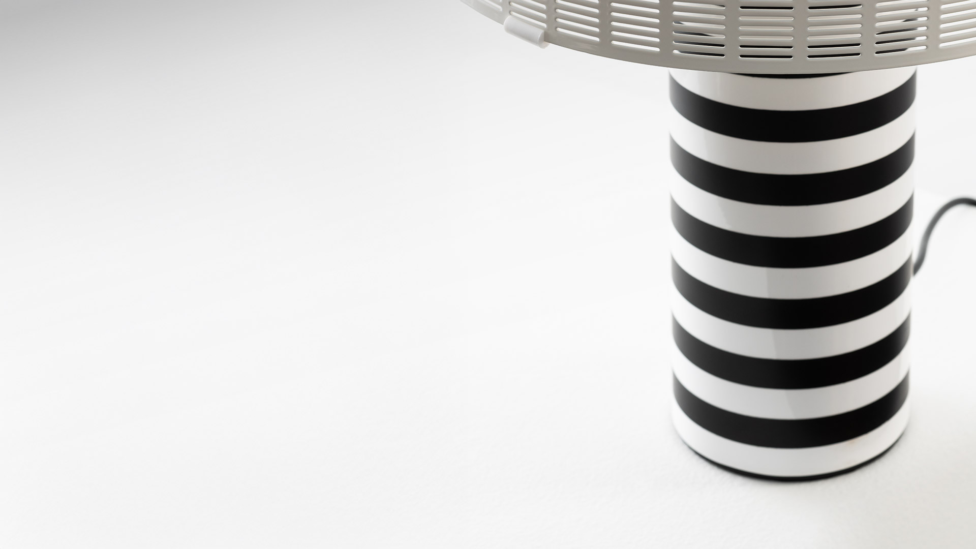 Lampada da tavolo Artemide Shogun con paralume semicircolare dorato a listelli e base cilindrica a strisce bianche e nere su piedistallo scuro