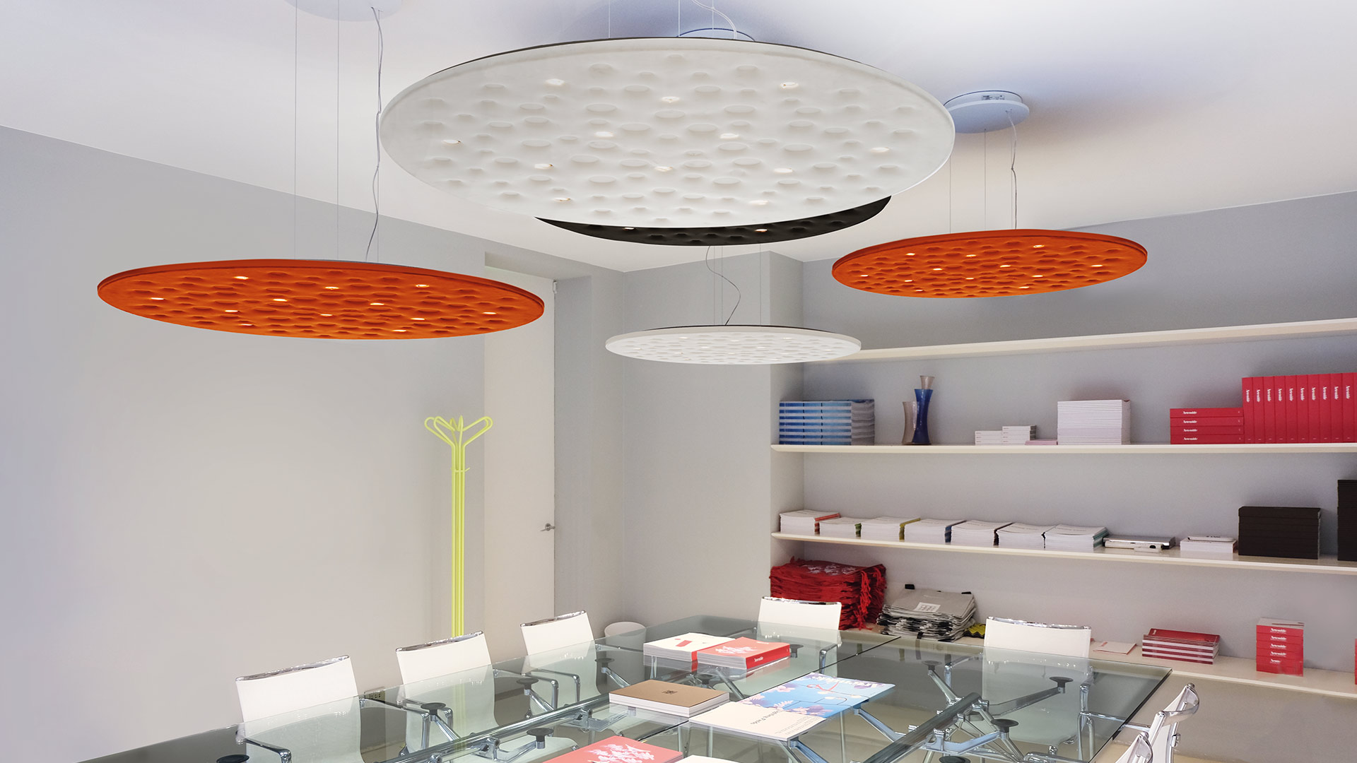 Two Artemide Silent Field 2.0 red pendant lamps illuminate a modern open-plan office with workstations and iMac computers.
