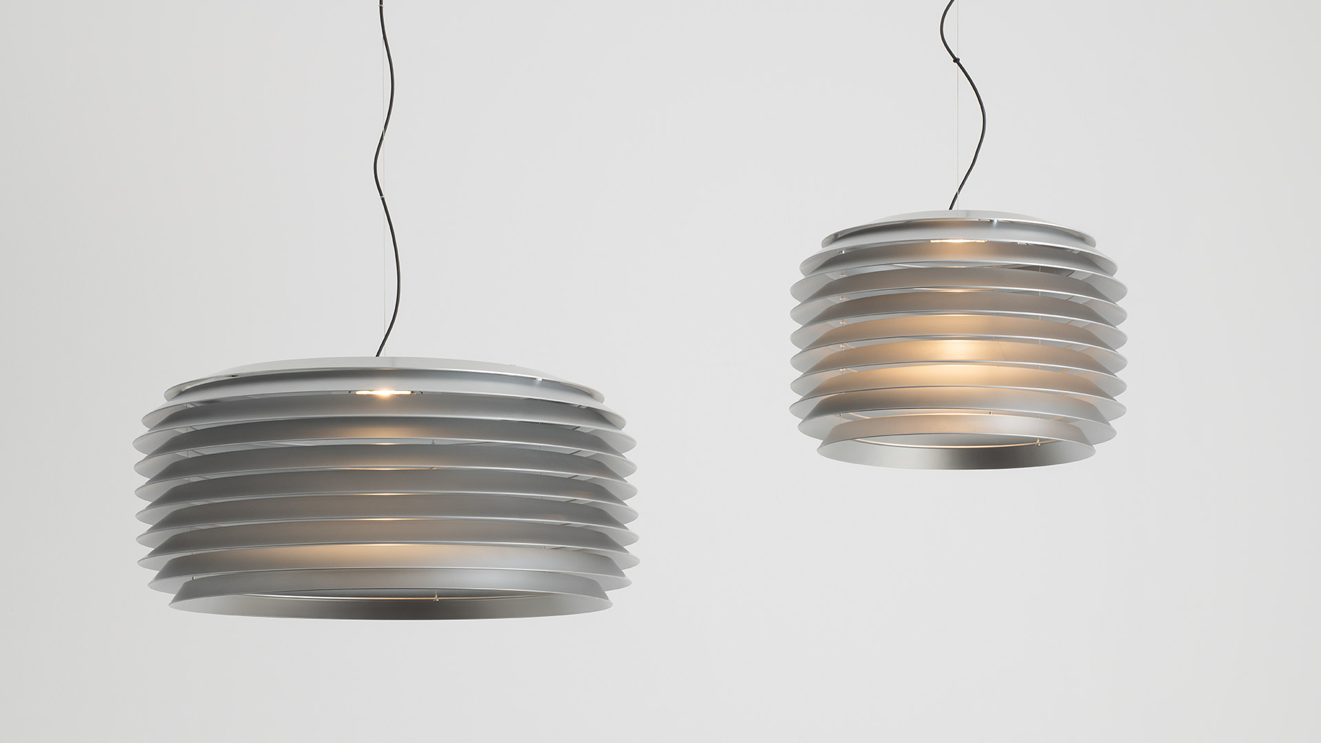 Lampada a sospensione Artemide Slicing con paralume grigio a strati sopra un tavolino rotondo arancione con oggetti decorativi.