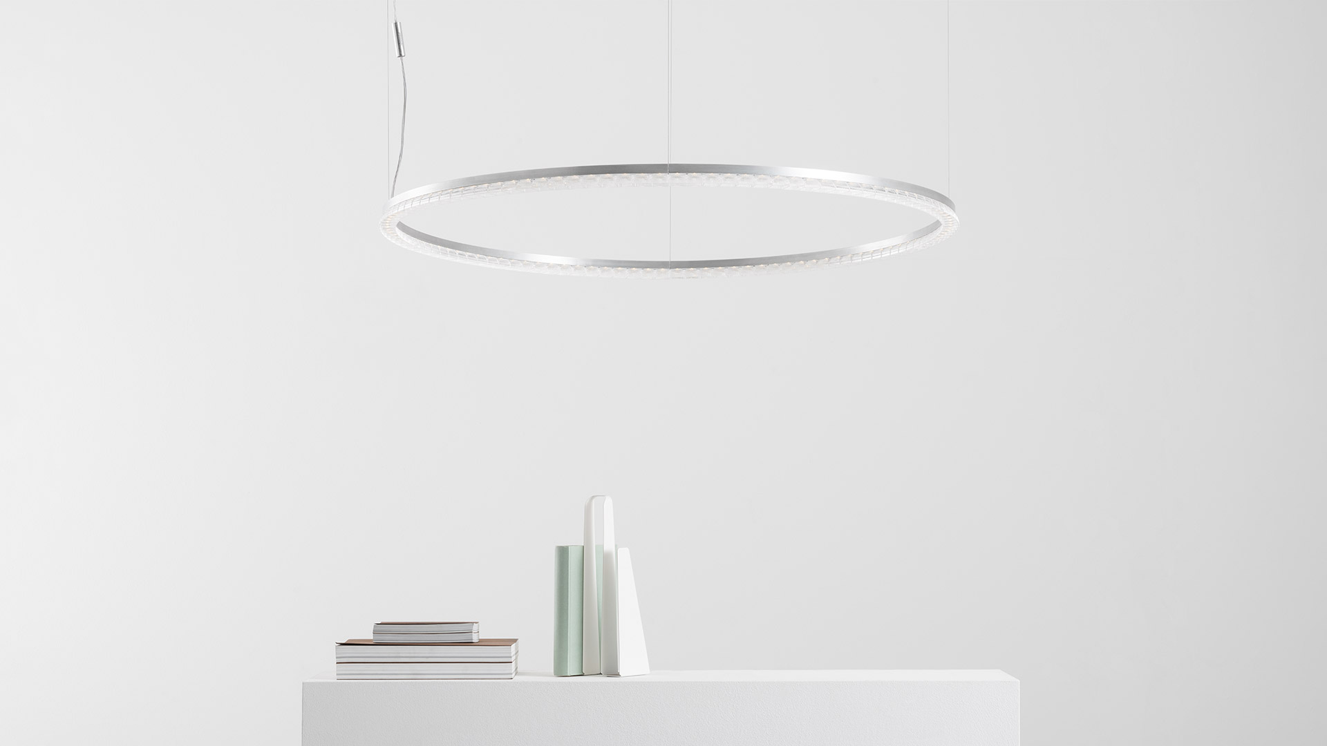 Lampada a sospensione Artemide Somnĭum: grande anello LED circolare bianco sospeso da sottili cavi sopra una mensola bianca minimalista