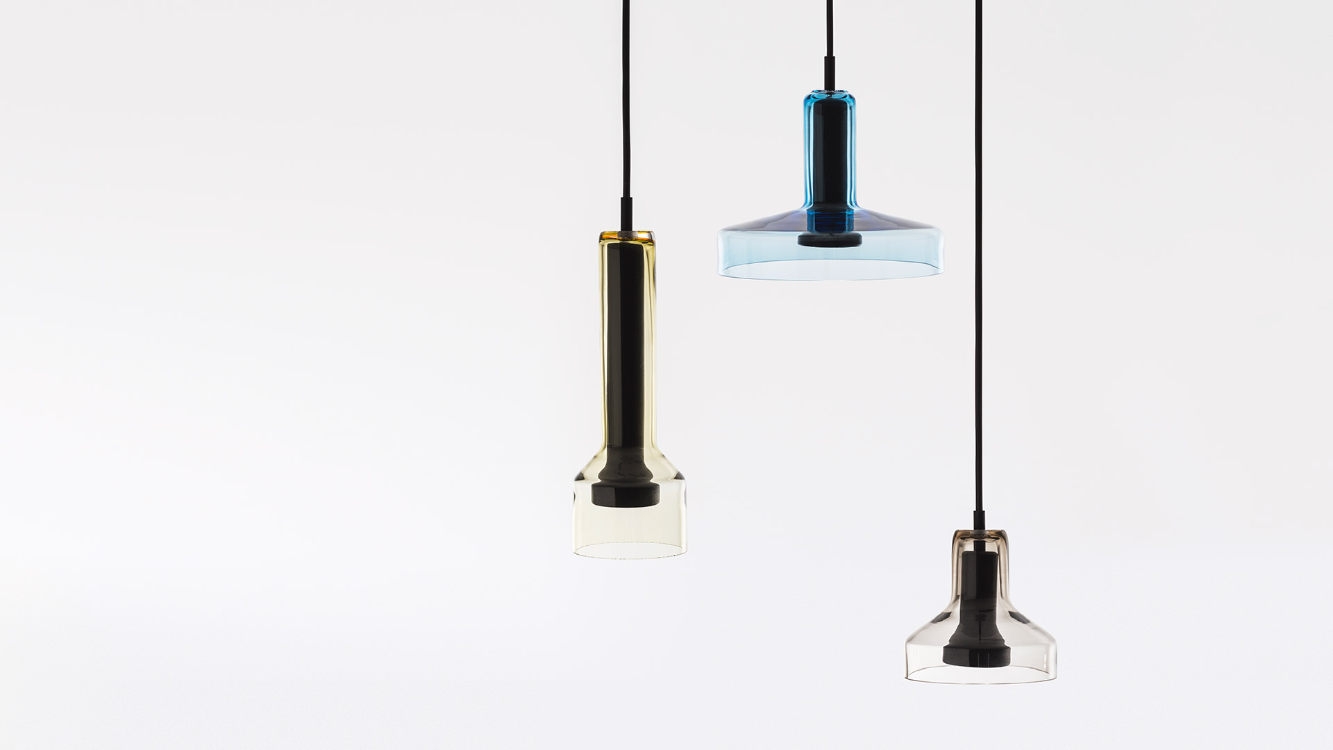 Tre lampade a sospensione Artemide Stablight con diffusori in vetro blu appese a diverse altezze da una rosetta nera a soffitto su cavi neri