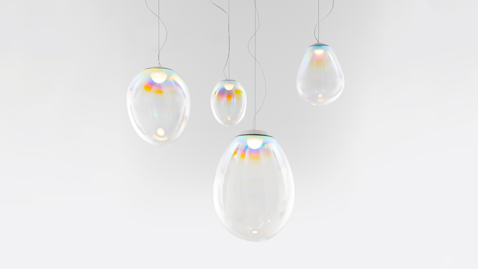 Artemide Stellar Nebula: tre lampade a sospensione in vetro iridescente con sfumature arcobaleno, sospese a diverse altezze da un rosone circolare