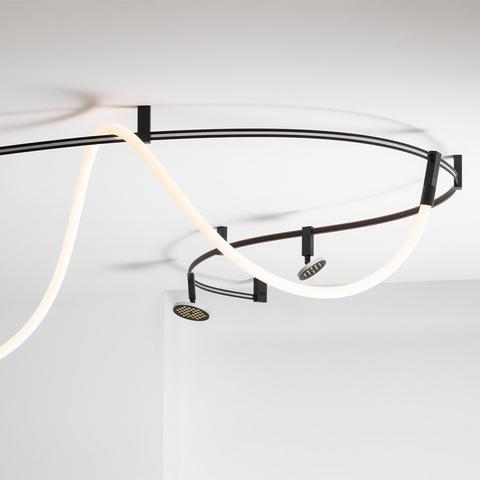Lampada da soffitto Artemide Sylt: binario curvo in metallo scuro con striscia LED bianca luminosa e due faretti orientabili a soffitto