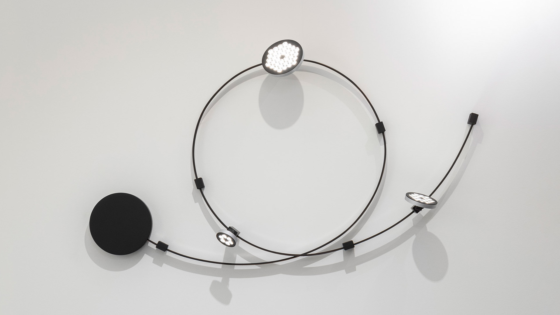 Sistema Artemide Sylt: illuminazione a binario modulare nera con lampadine a sospensione, configurazioni circolari e curve su soffitto e parete