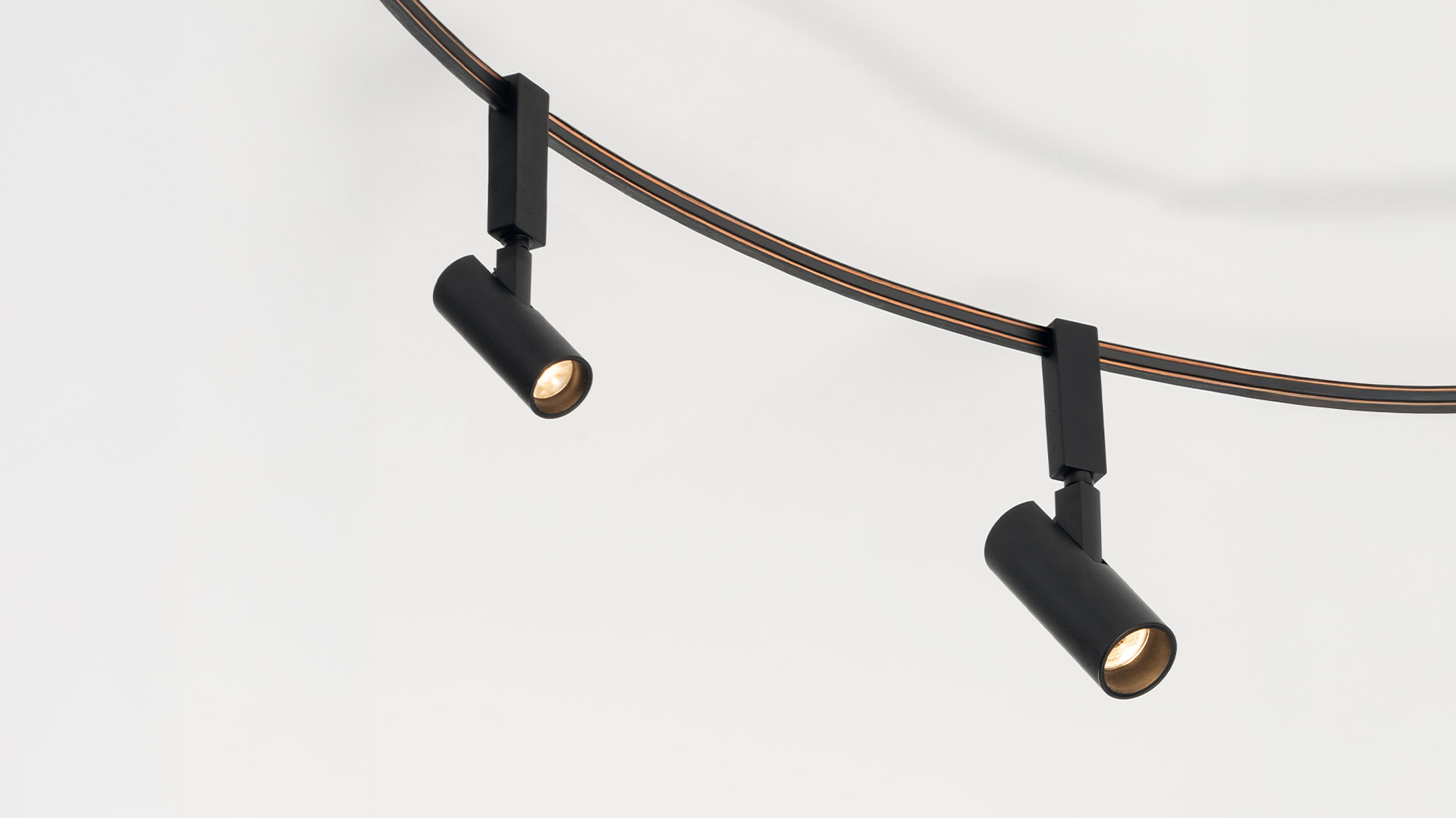 Due mani che piegano un cavo scuro flessibile a forma di anello, dimostrando la struttura regolabile della lampada Artemide Sylt