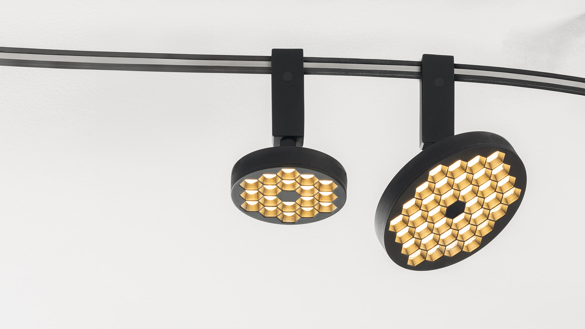 Due faretti Artemide Sylt su binario nero opaco con array LED a nido d'ape dorato, montati su sistema a binario curvo nero