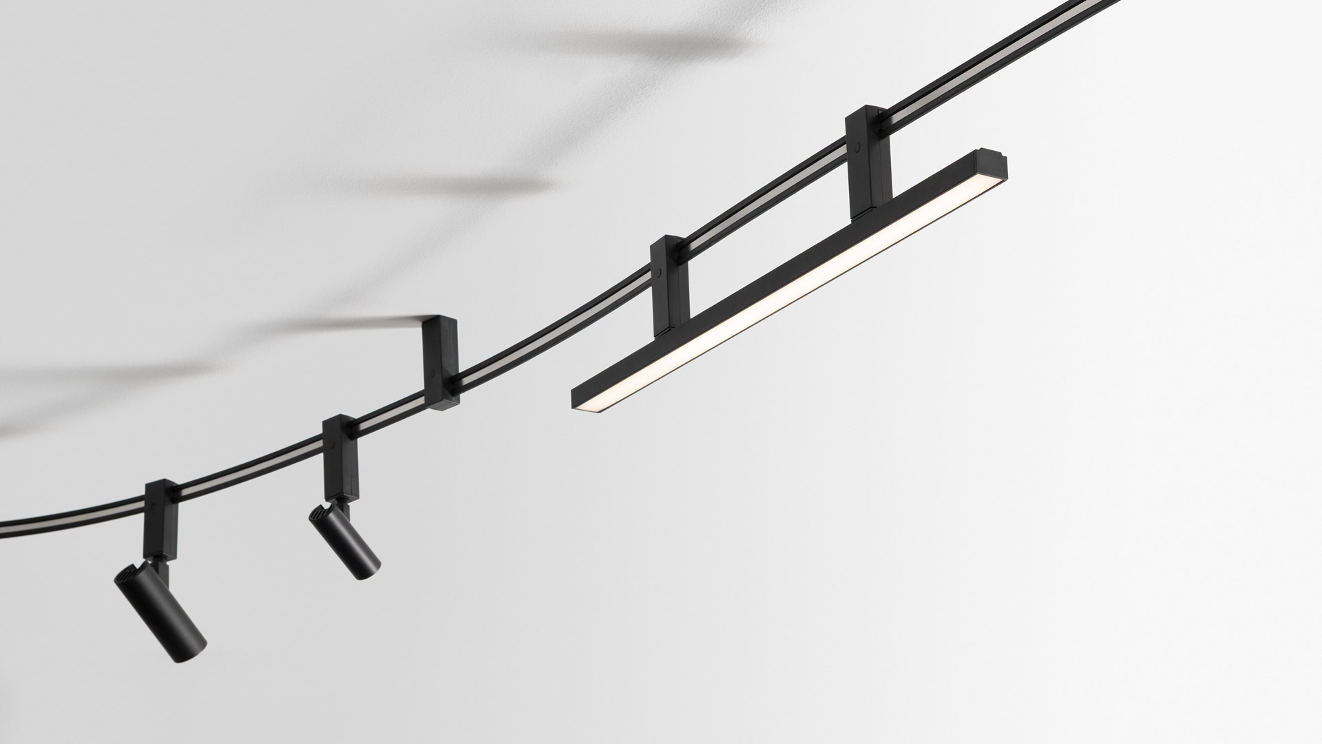 Sistema soffitto Artemide Sylt: due faretti LED circolari neri montati su cavi curvi neri con staffe quadrate a soffitto