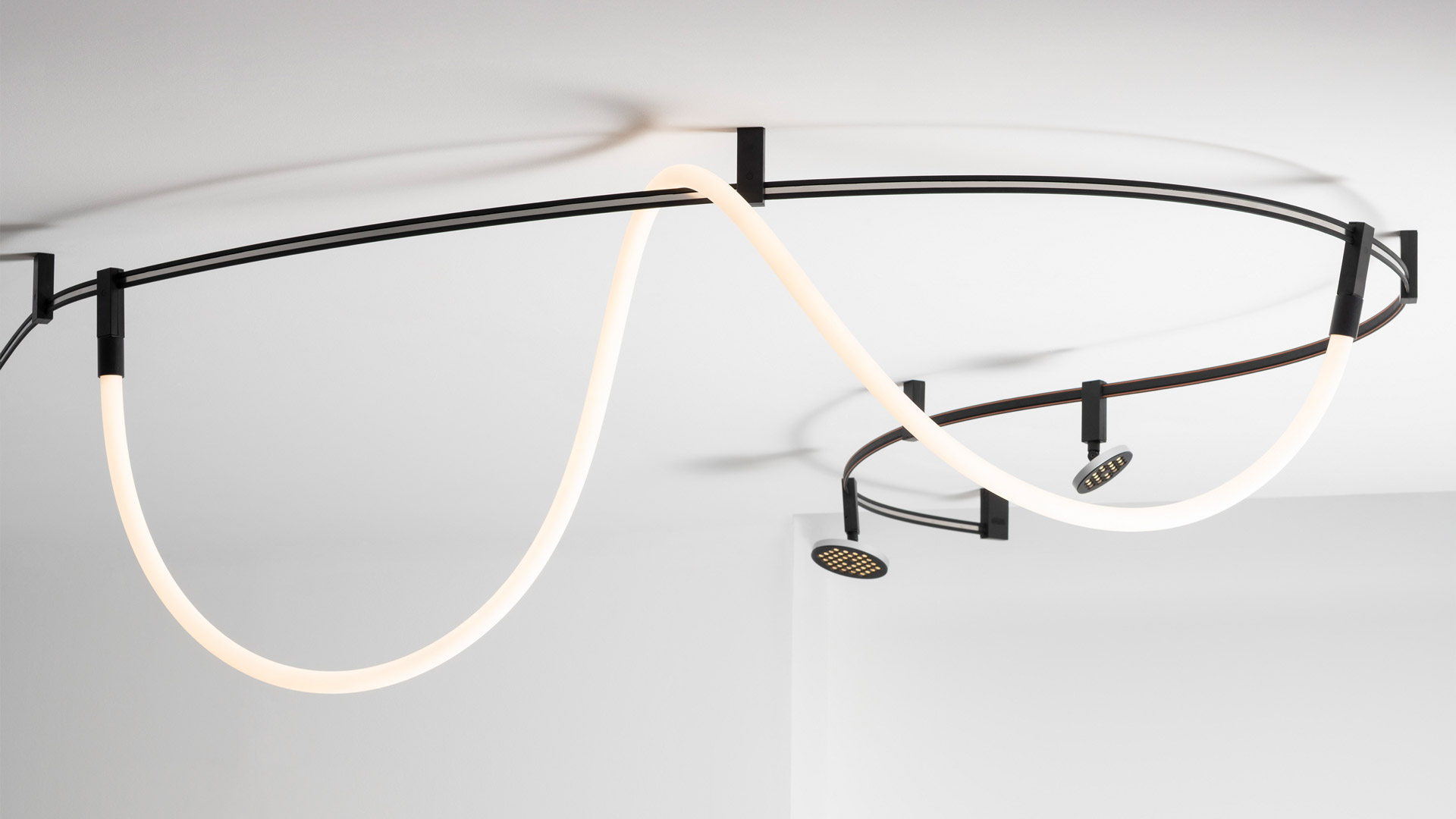 Tre lampade a sospensione Artemide Sylt con sfere in vetro opalino appese a diverse altezze da una guida curva a soffitto su sottili cavi neri