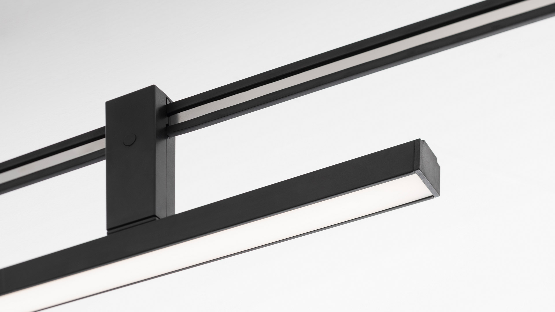 Sistema Artemide Sylt: binario curvo nero a soffitto con più sospensioni tra cui paralumi cilindrici, sferici in vetro, una goccia in ottone e un tubo LED flessibile
