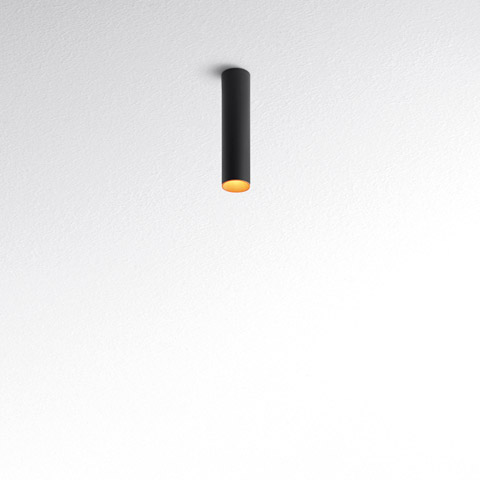 Tagora Soffitto 80 ceiling spotlight by Artemide: slim black cylindrical body with warm gold interior, surface-mounted on white ceiling