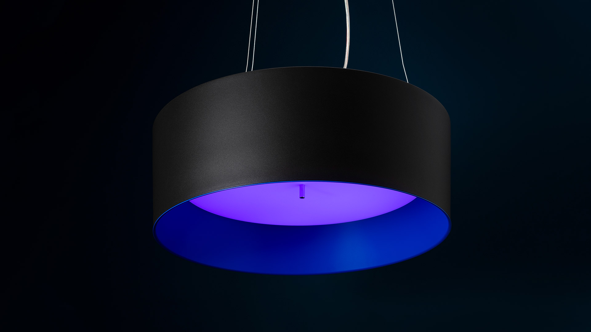 Lampada a sospensione Artemide Tagora Sospensione 570 con paralume cilindrico nero opaco che emette luce blu-viola vivida dall'interno