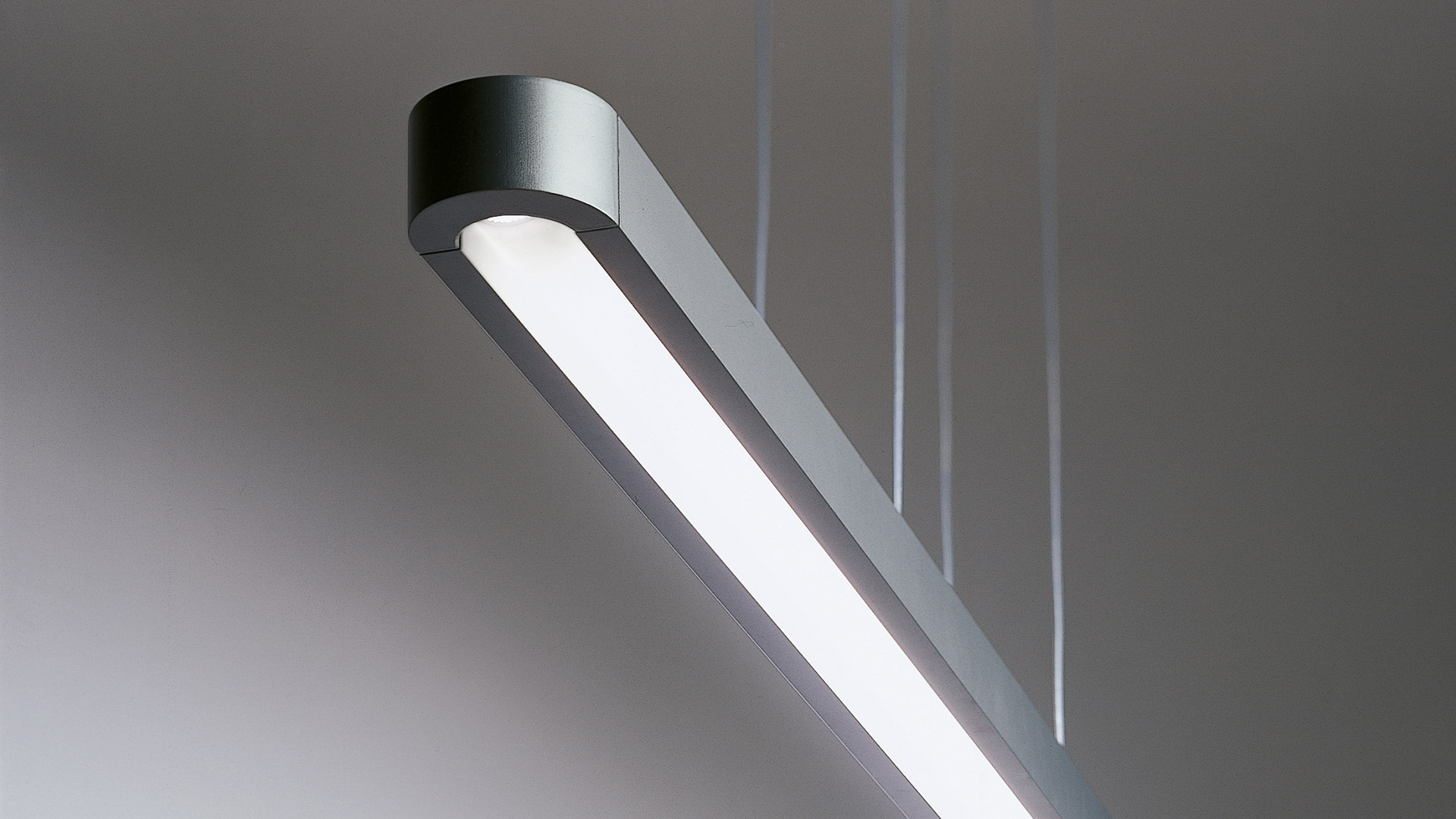 Lampada a sospensione Talo di Artemide: corpo lineare allungato bianco con LED e bordi arrotondati, emette luce calda verso il basso