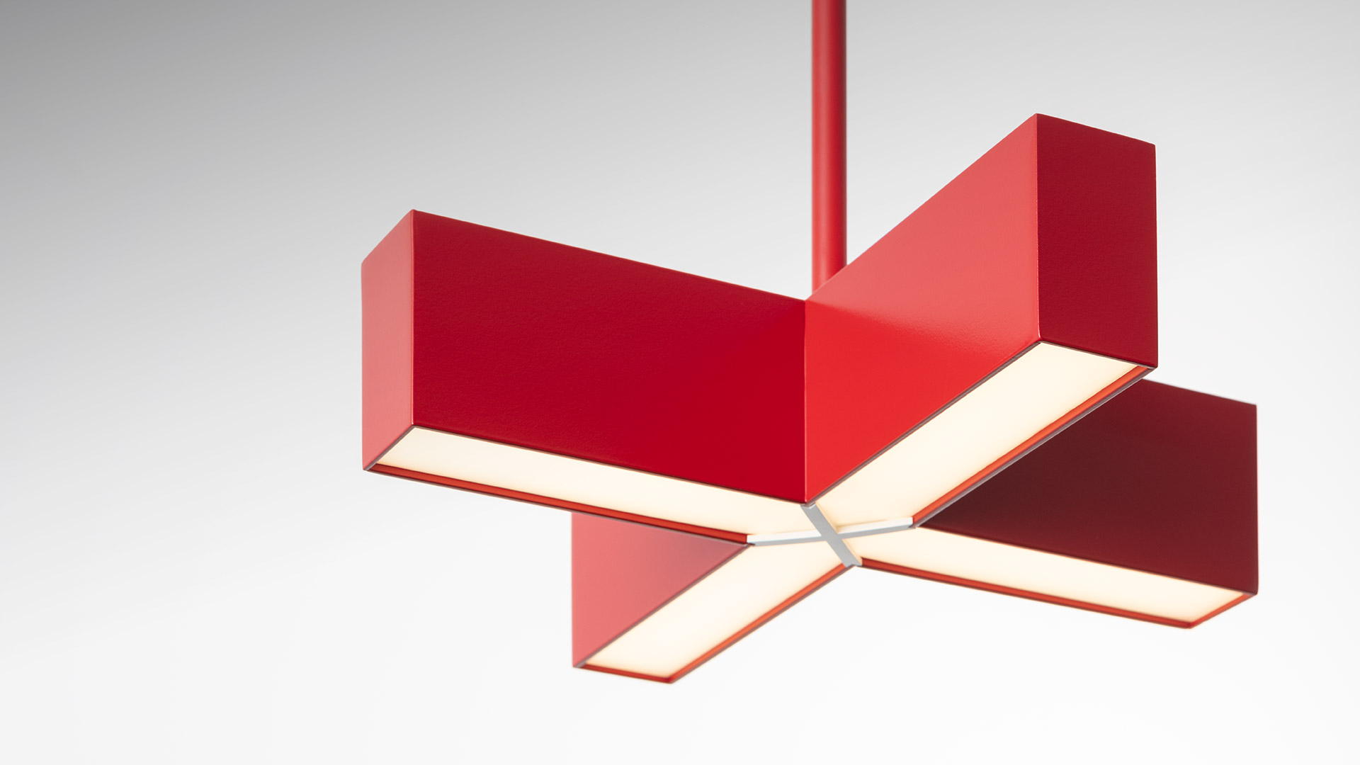 Artemide Tetras pendant lamp in red, featuring four rectangular LED arms arranged in a cross shape, emitting warm diffused light