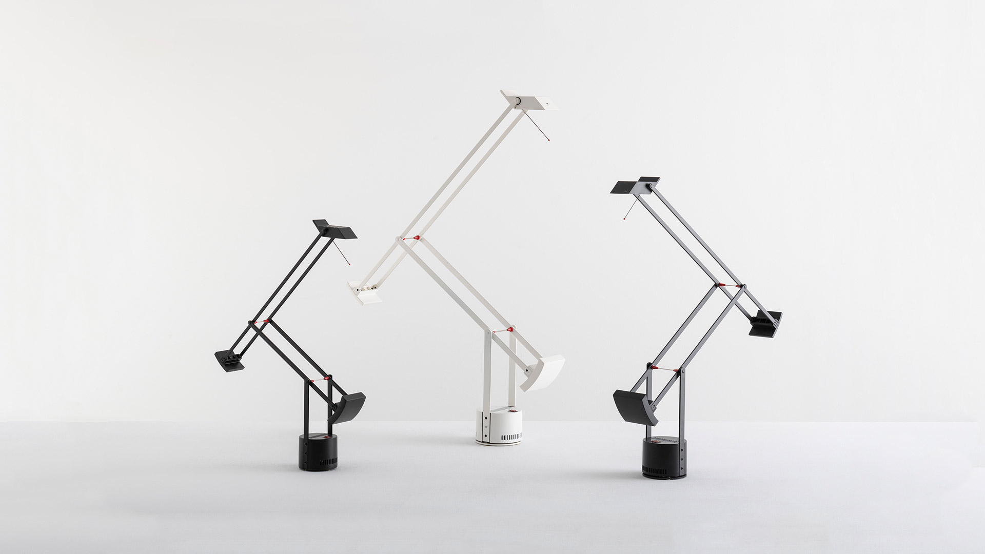 Interno di boutique elegante con due lampade da tavolo Artemide Tizio nere, poste su piedistalli verdi e una cassettiera rosa, vicino a finestre ad arco.