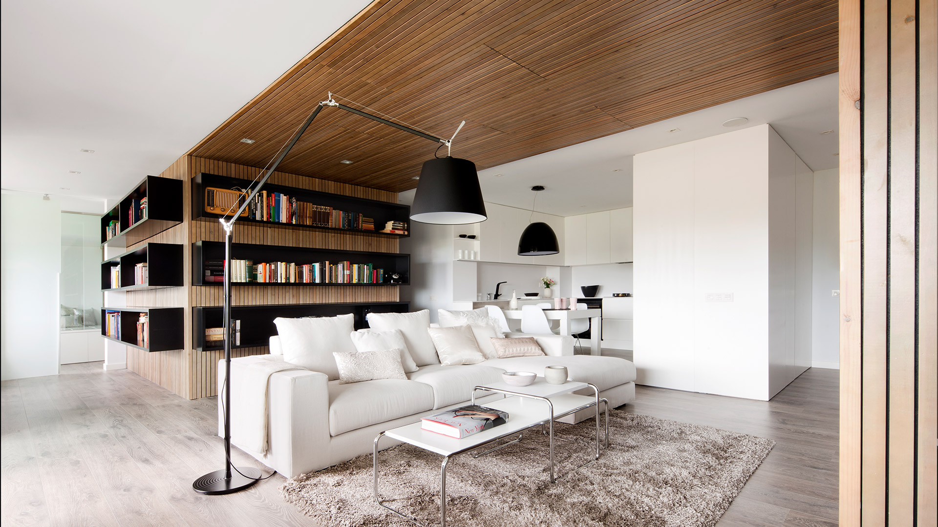 Soggiorno moderno con lampada da terra Artemide Tolomeo Mega Terra accanto a un divano bianco, soffitto in legno e libreria a muro.