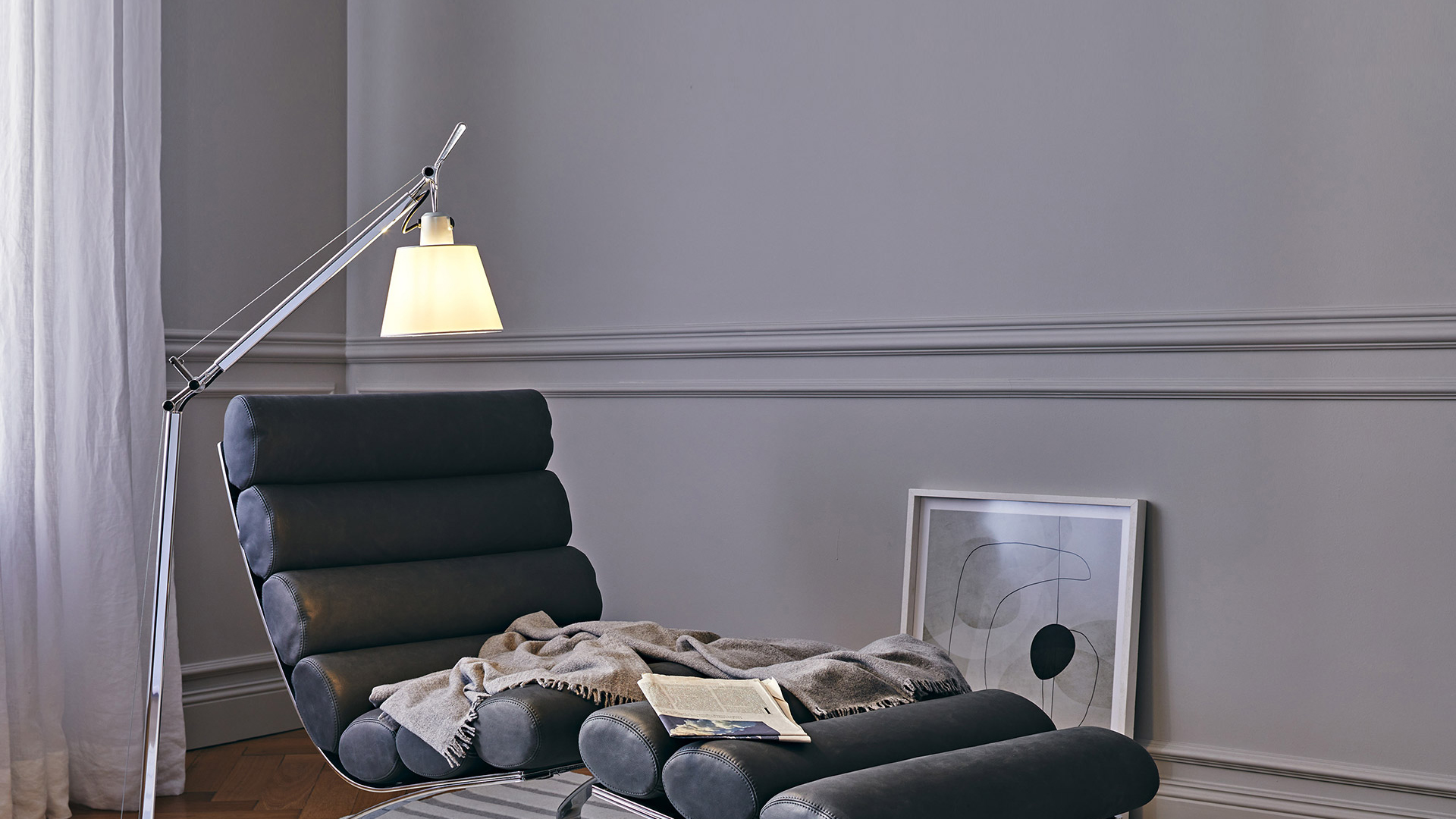 Lampada da terra Artemide Tolomeo Basculante con braccio in alluminio illumina una chaise longue scura in un'elegante stanza grigia