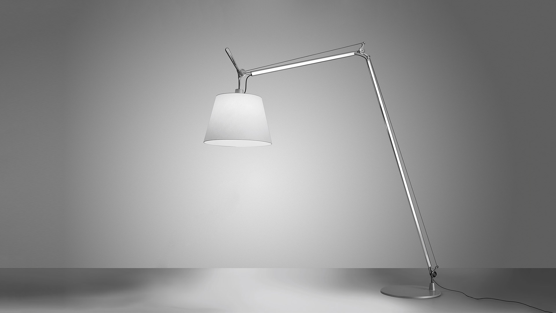 Lampada da terra Artemide Tolomeo Maxi con braccio articolato in alluminio e ampio paralume conico bianco, che diffonde luce calda su sfondo neutro