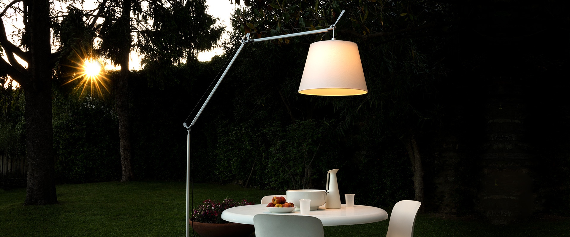 Lampada da terra Artemide Tolomeo Paralume Outdoor con paralume bianco che illumina un tavolo da pranzo in giardino al tramonto