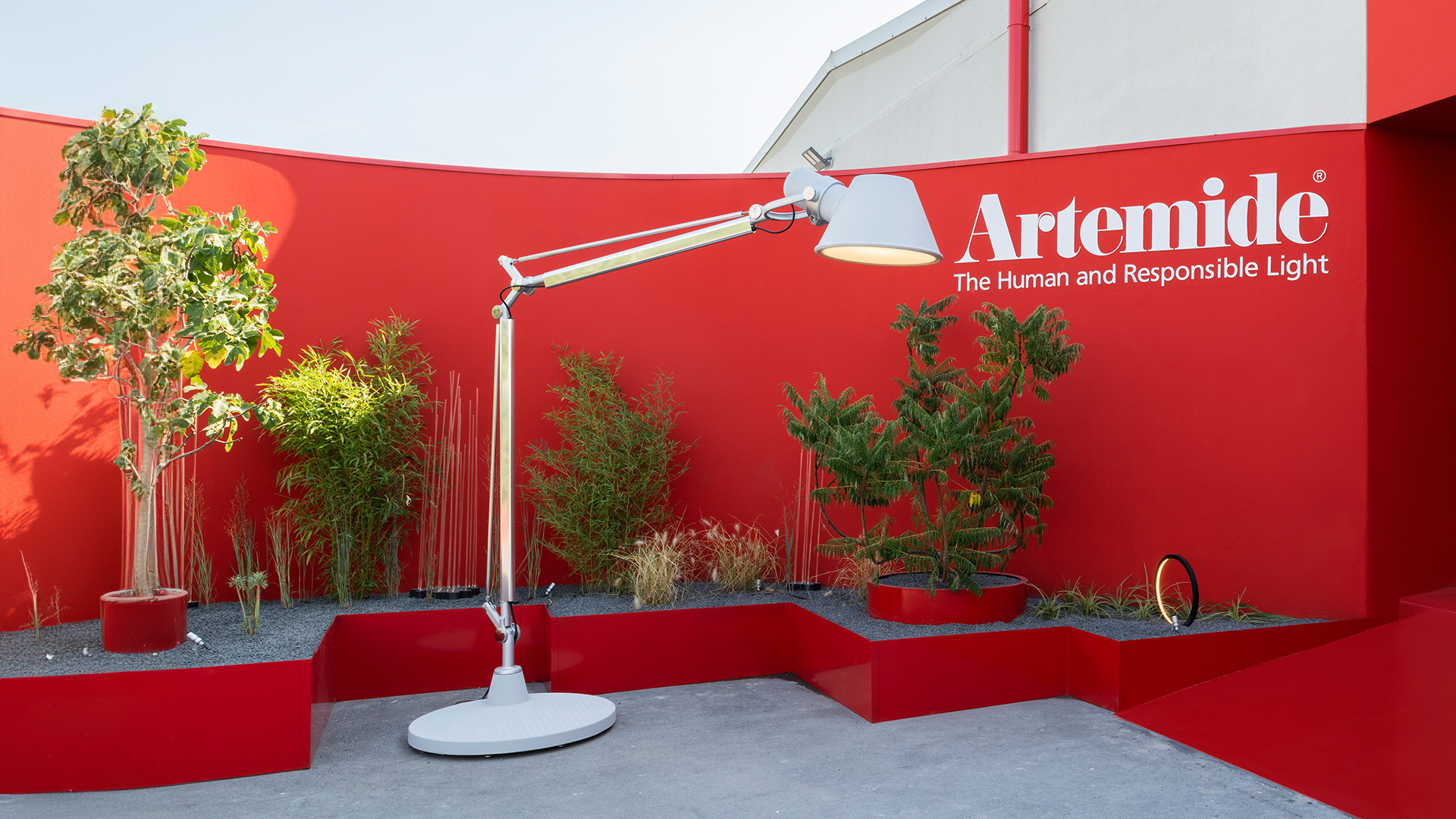 Lampada da terra Artemide Tolomeo XXL Outdoor su un moderno deck in legno al crepuscolo, con sedute modulari bianche e padiglione con pareti in vetro