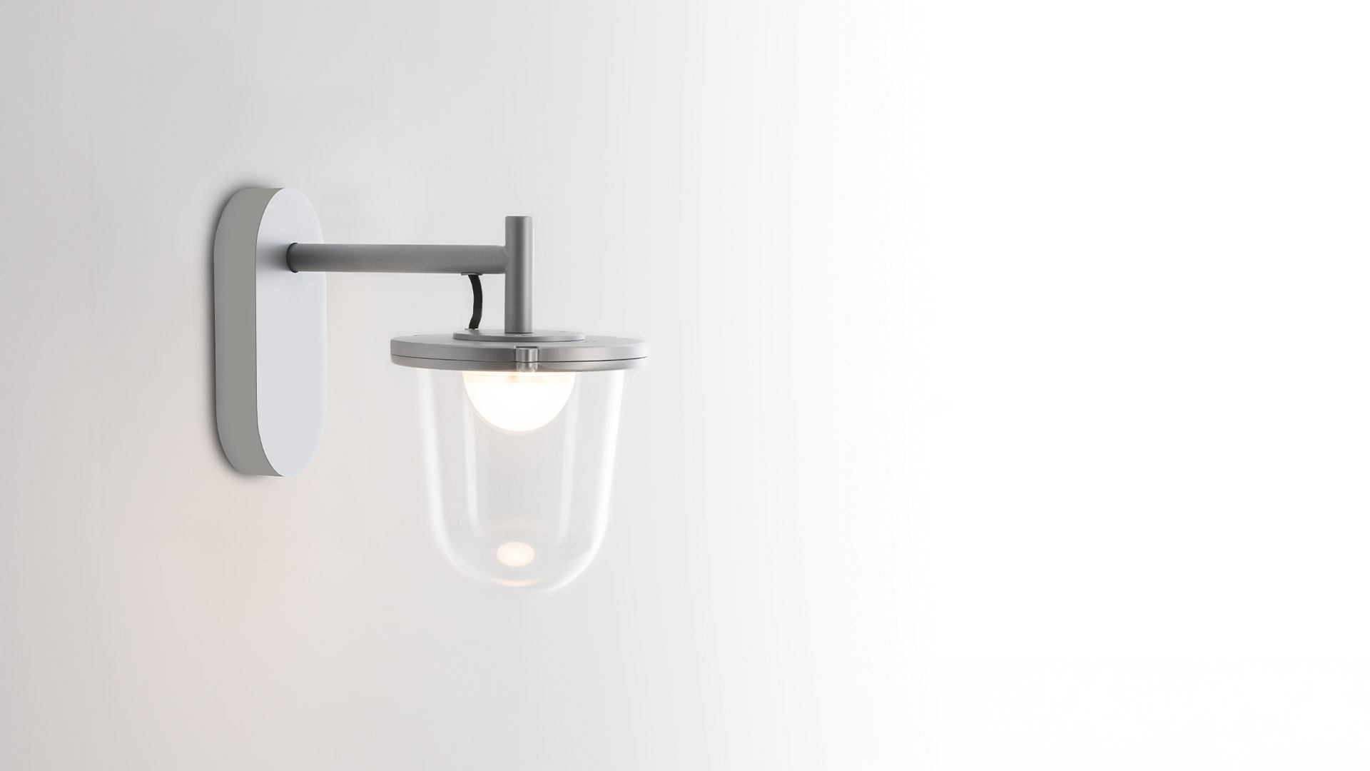 Lampada a sospensione Tolomeo Lampione Outdoor di Artemide: paralume a campana in vetro trasparente con gancio metallico, mostrata all'esterno e in studio