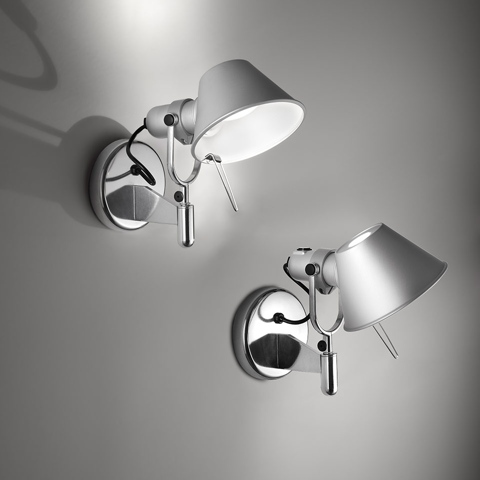 Two Artemide Tolomeo wall lamps in aluminium: left Parete with shade facing up, right Faretto with adjustable arm, both on round wall mounts.