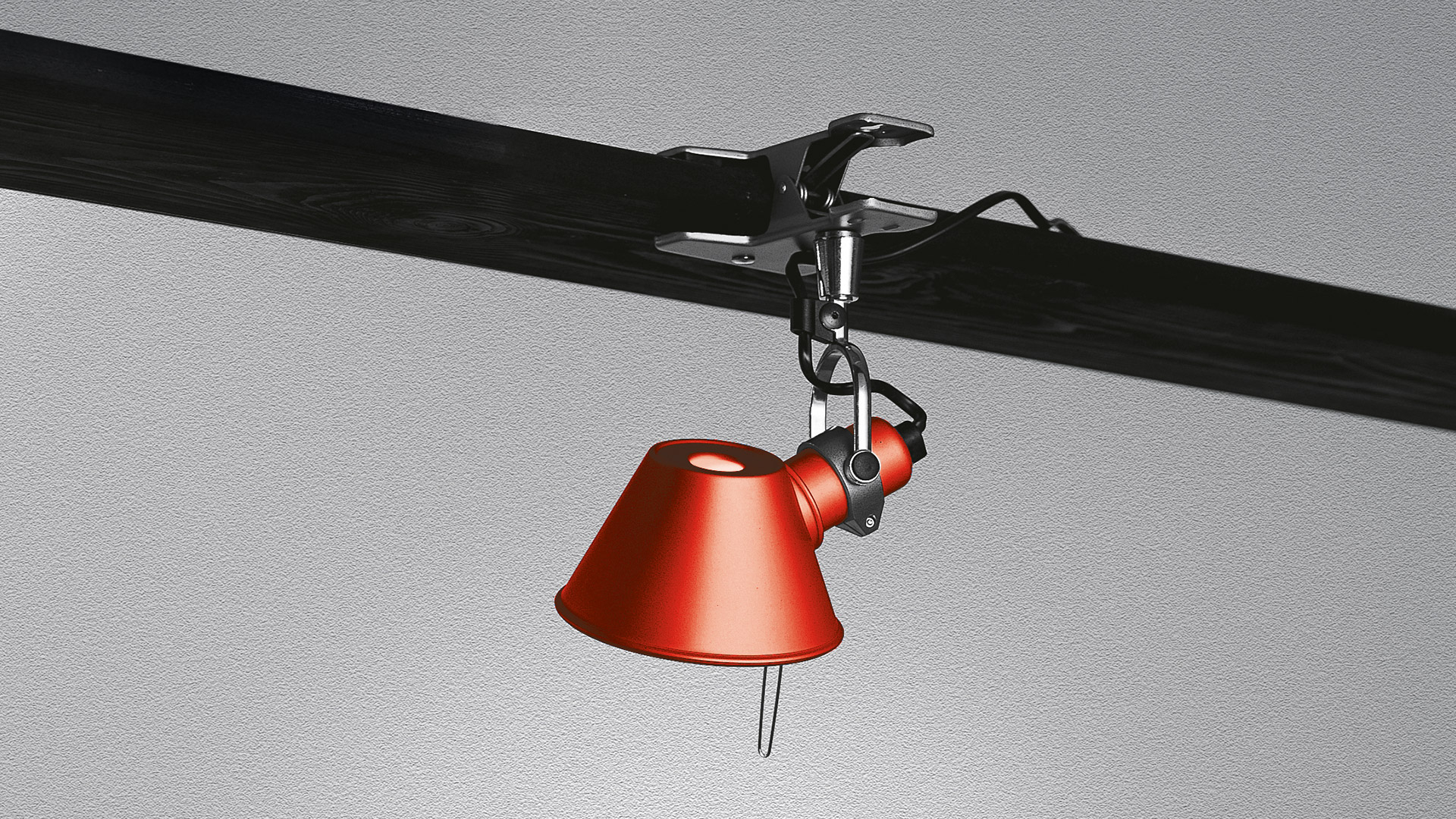 Lampada a morsetto Artemide Tolomeo Pinza in rosso, fissata a una trave scura, con braccio regolabile e paralume conico rivolto verso il basso