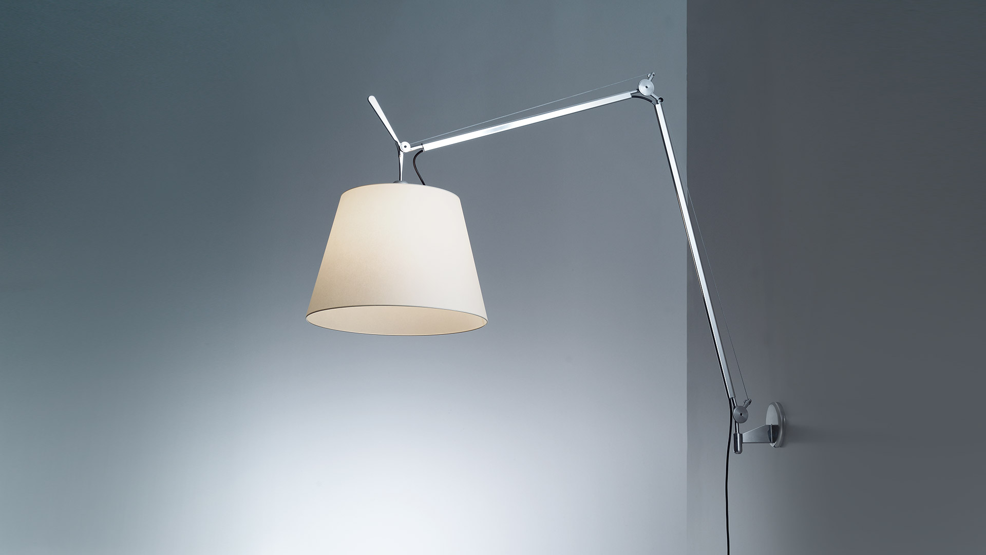 Lampada da parete Artemide Tolomeo Mega Parete con braccio regolabile in alluminio e ampio paralume conico color pergamena, montata su parete grigia