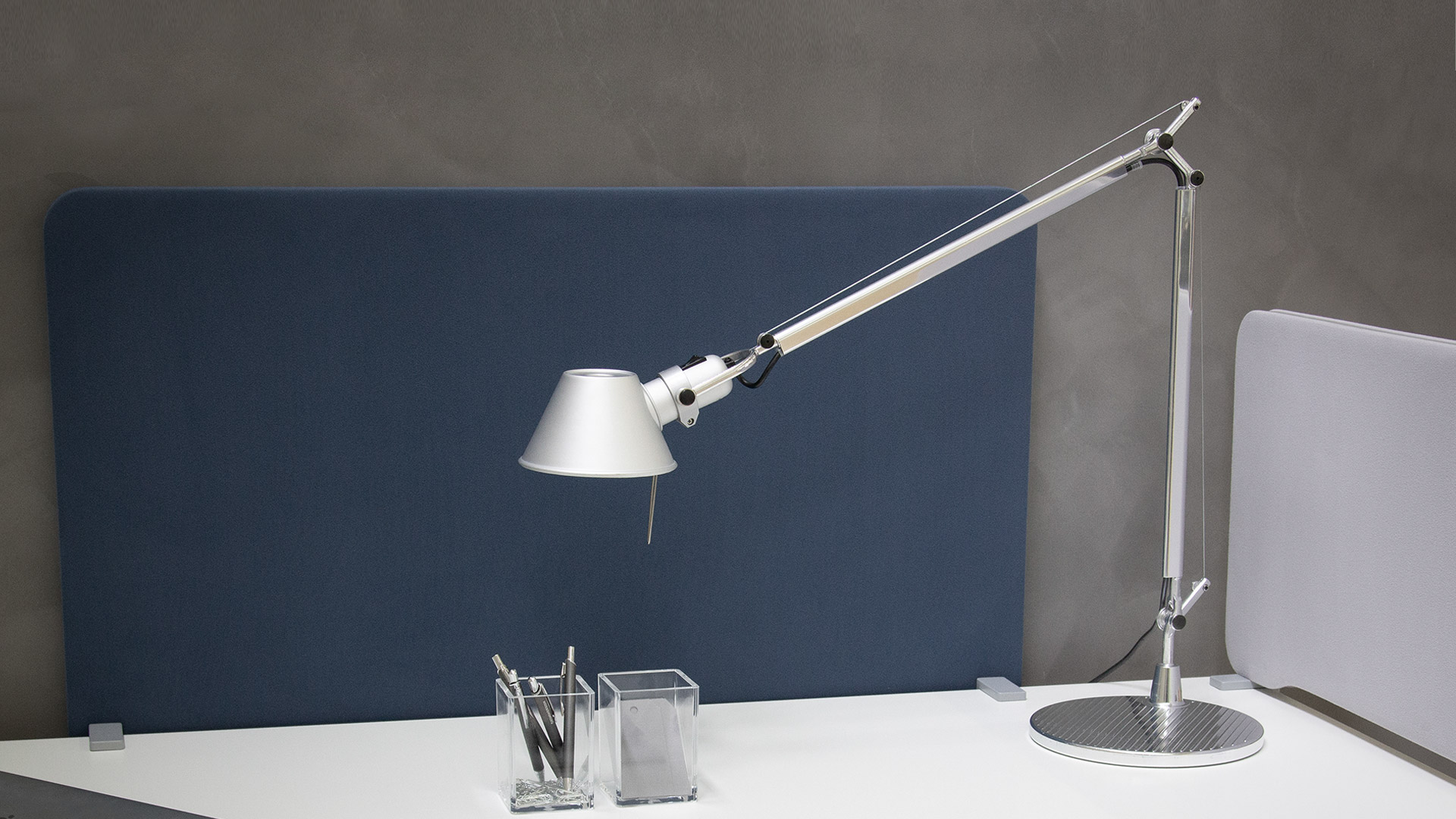 Four Artemide Tolomeo Tavolo desk lamps in silver and white finishes, various sizes, with adjustable arms on circular bases, against yellow background