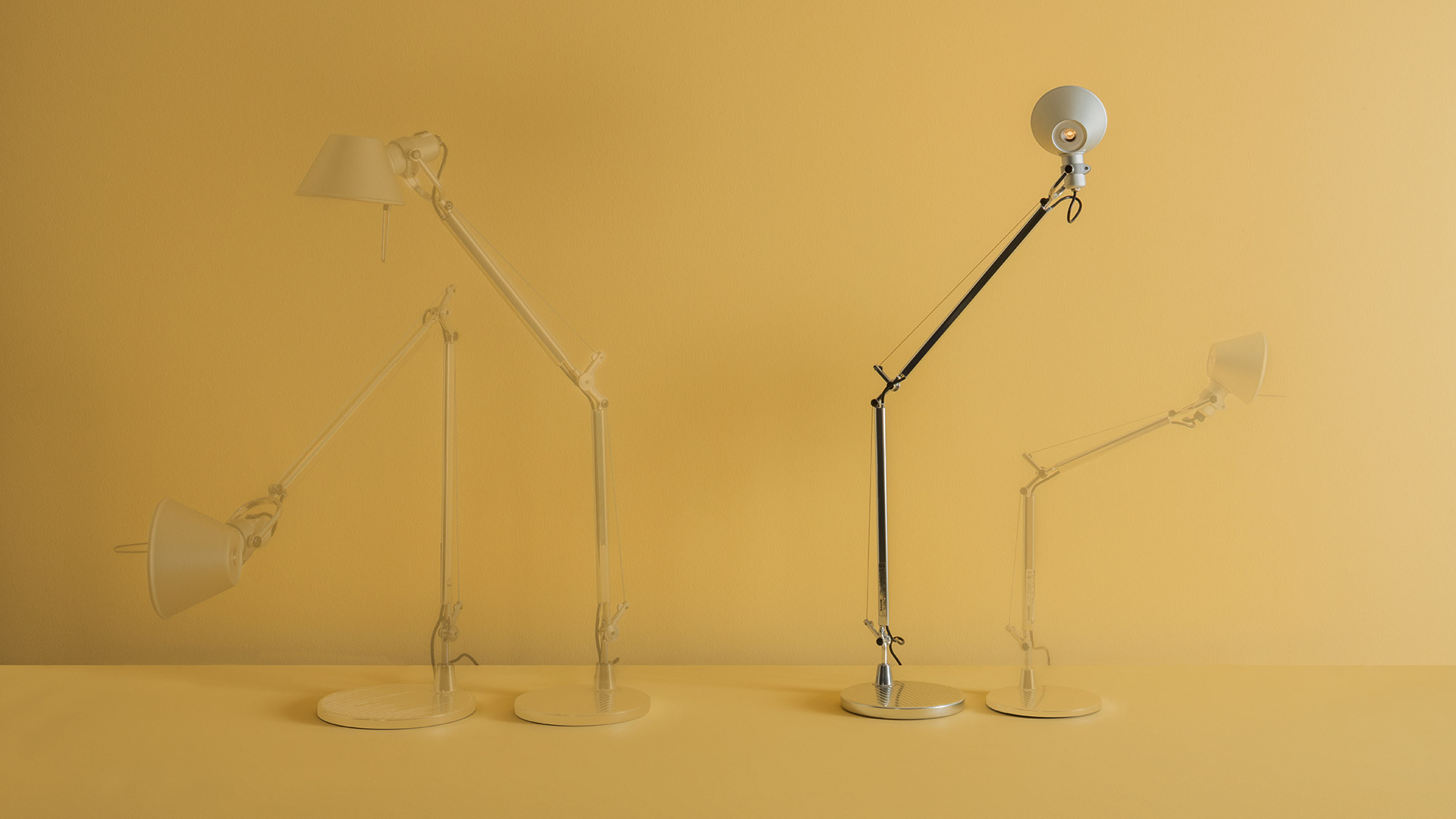 Four Artemide Tolomeo desk lamps: two white Tolomeo Tavolo on left, two chrome Tolomeo Midi Tavolo on right, yellow background