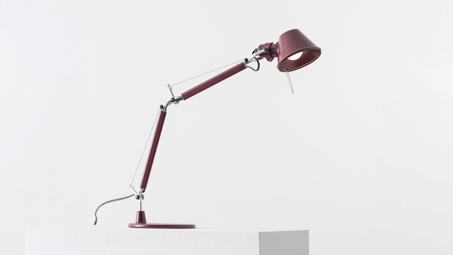 Artemide Tolomeo Micro Tavolo white desk lamp with articulated arm on a minimalist workspace with laptop, notebook, and stationery
