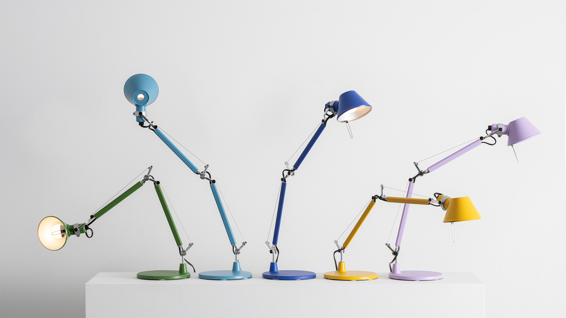 Four Artemide Tolomeo desk lamps: three white Tolomeo Tavolo and one chrome Tolomeo Micro Tavolo on a yellow background