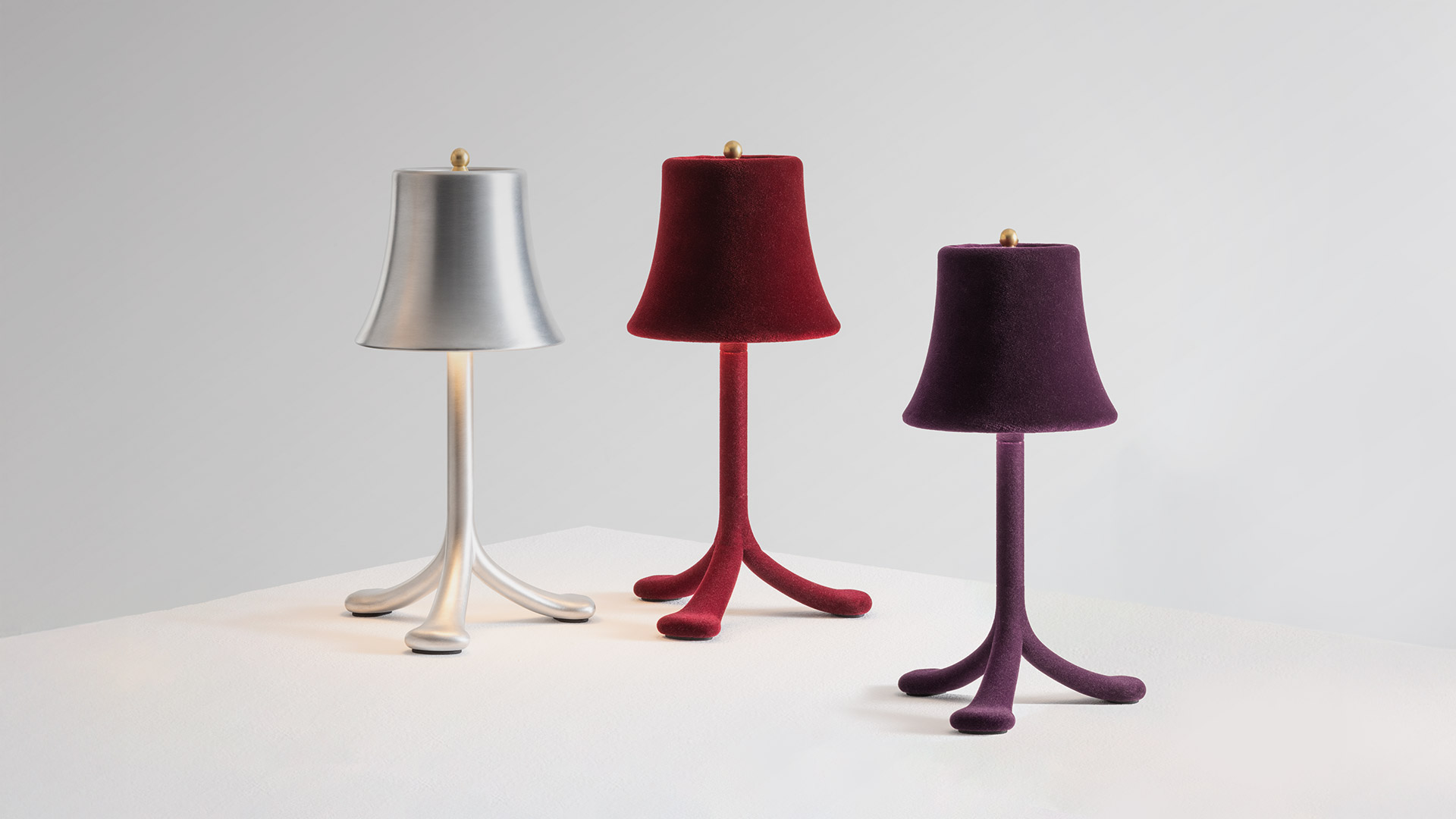 Lampada da tavolo Trois Rois di Artemide: dettaglio paralume in alluminio spazzolato con finale dorato e mano che regge la versione portatile con stelo flessibile