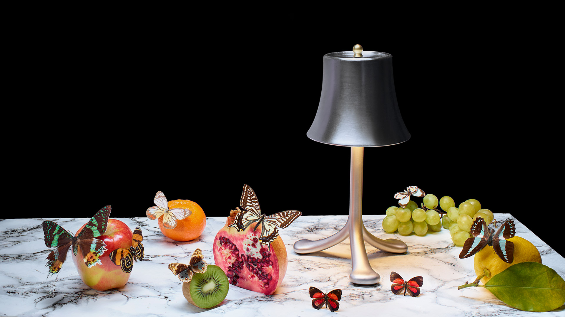 Lampada da tavolo Trois Rois di Artemide: paralume a campana argentato su base a tre gambe con luce calda, occhiali accanto