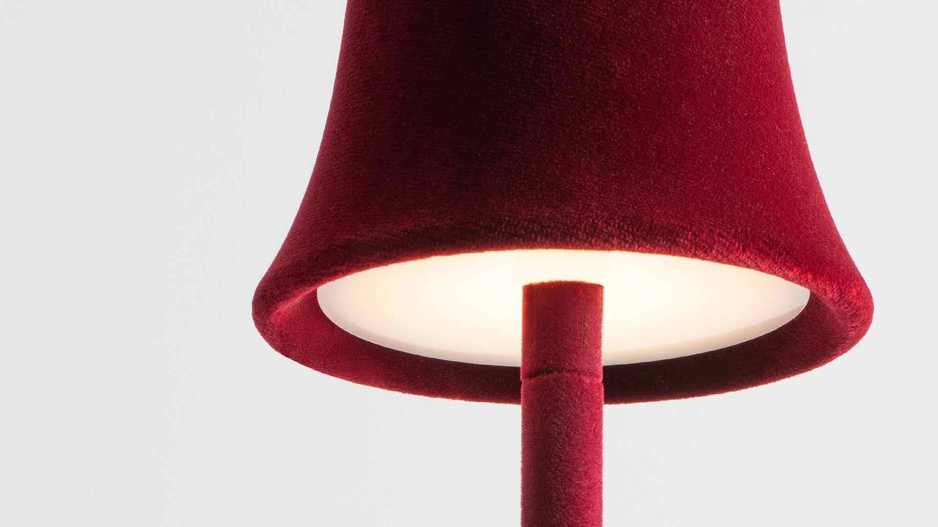 Lounge elegante con divani in velluto rosso, candele, camino e lampada da parete Artemide Trois Rois che diffonde calda luce ambrata vicino a un arco