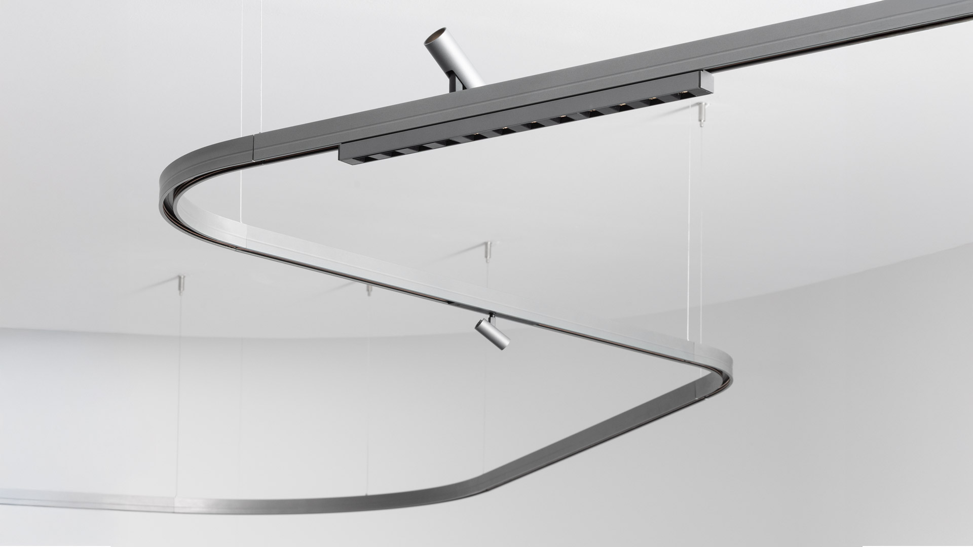 Artemide Turn Around System: lampada a sospensione tubolare ad anello grigio scuro che interseca una guida lineare, con due ugelli orientabili