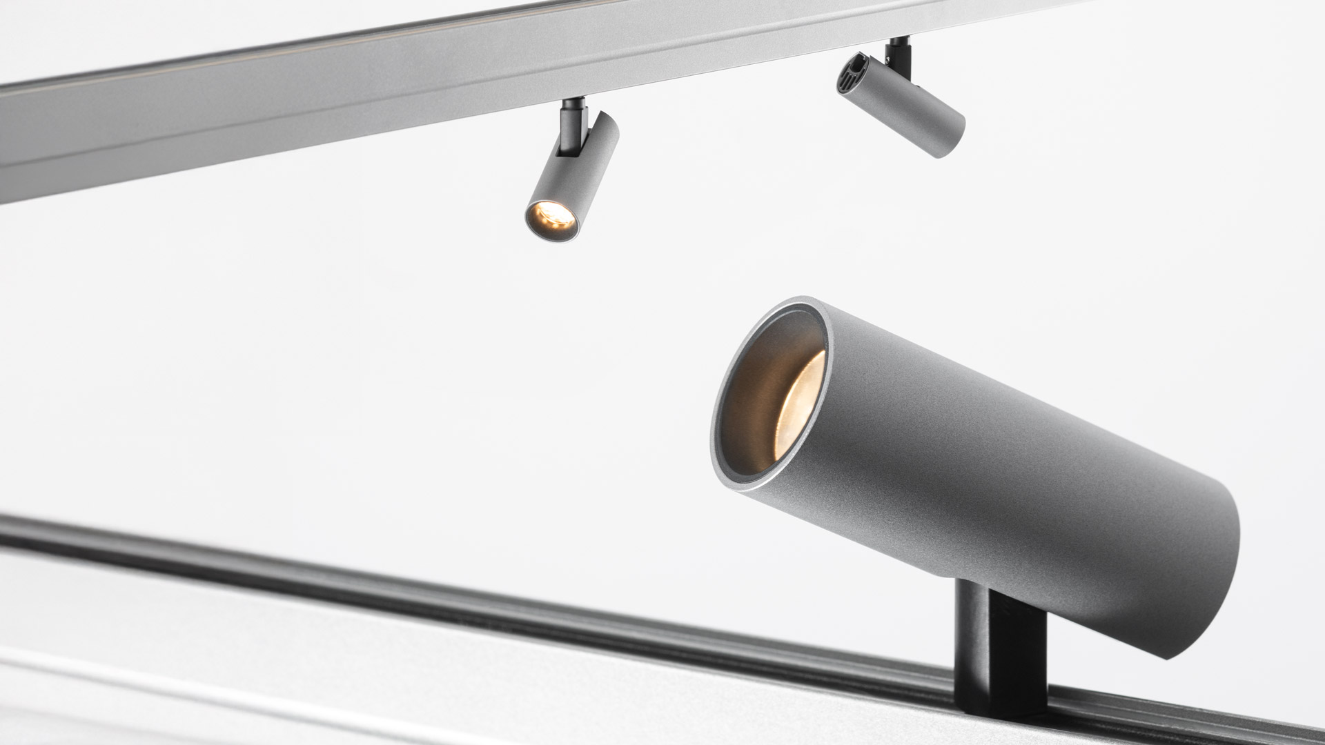 Artemide Turn Around System: faretto cilindrico argento su binario nero diagonale, con riflettore interno dorato caldo