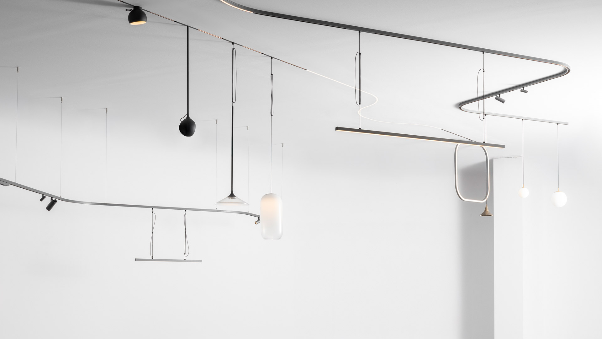 Sistema Artemide Turn Around: binario a soffitto nero con faretti, lampade a sospensione con diffusori in vetro e grande lampada circolare a parete