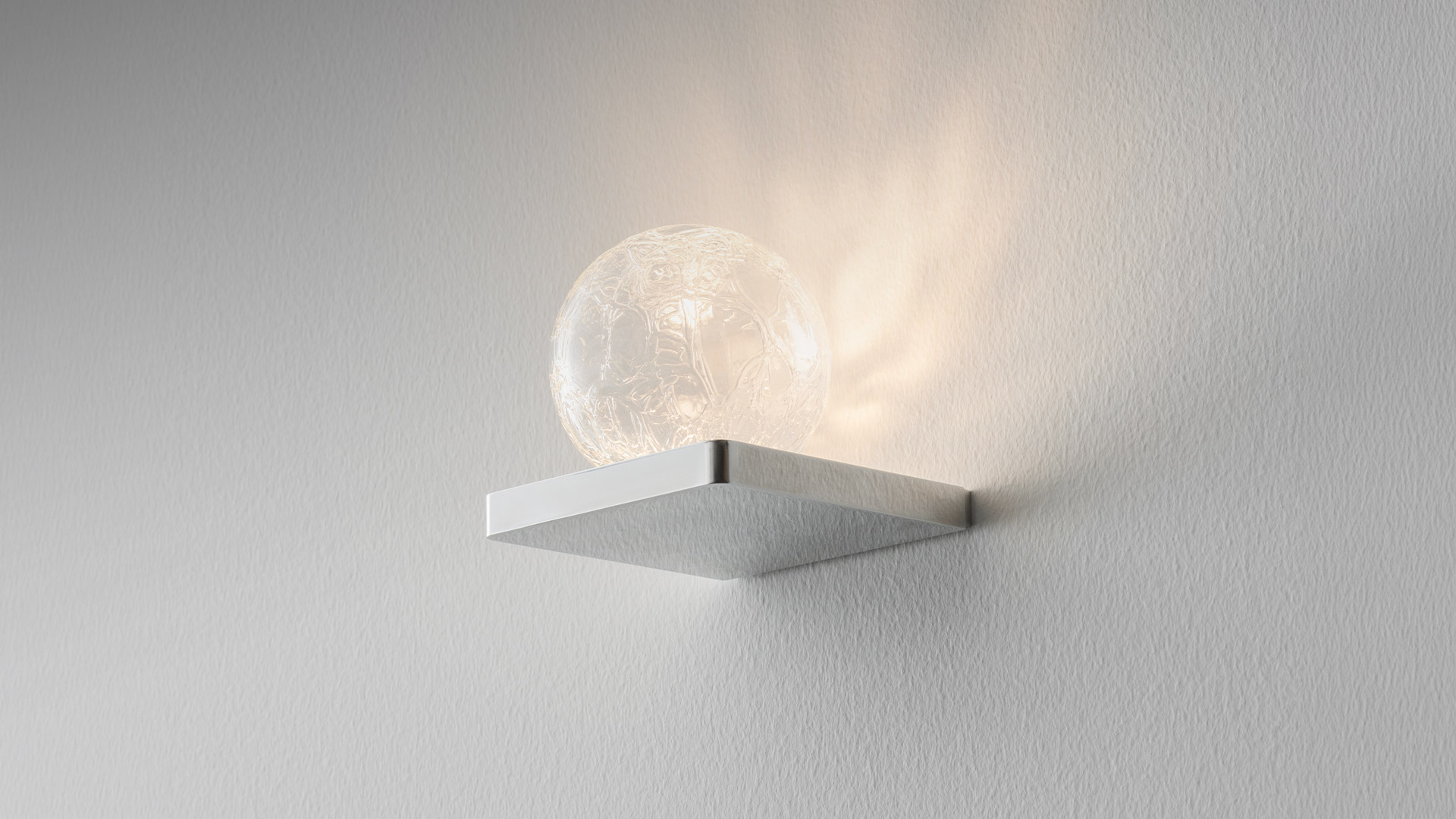 Primo piano di un diffusore sferico in vetro trasparente con intricata texture a rilievo organico, che crea una superficie scultorea diffondente luce