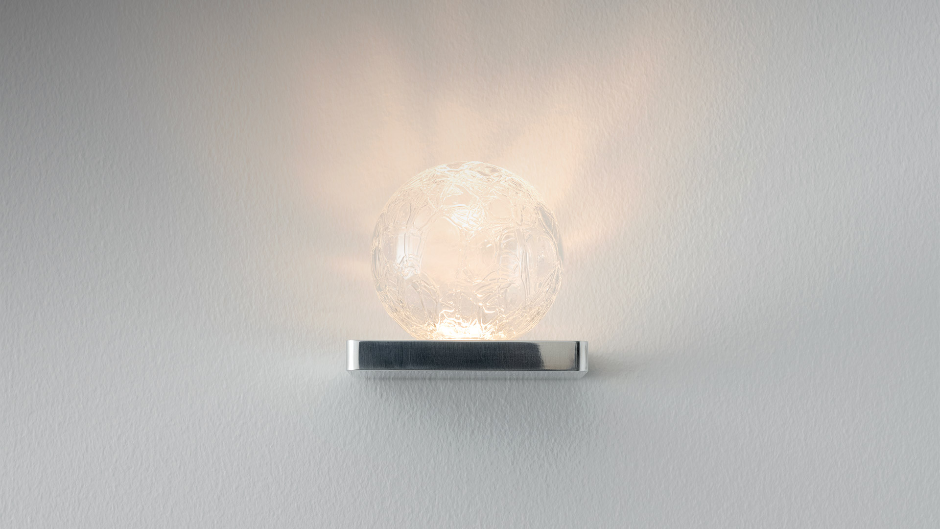 Applique Artemide Ulrich und Diotima: sfera in vetro lavorato su base rettangolare in cromo lucido, con luce diffusa calda