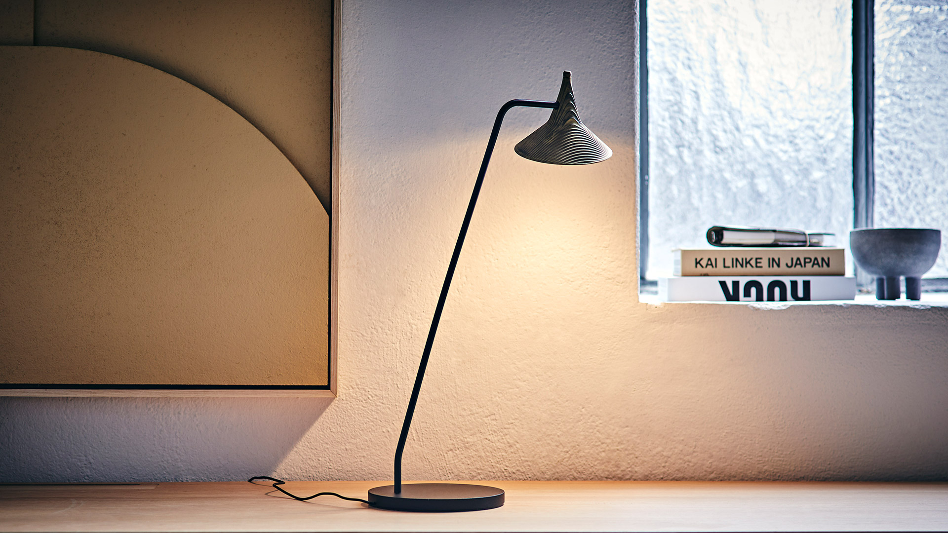 Lampada da terra Artemide Unterlinden: alta struttura in metallo nero con braccio regolabile che sospende un piccolo paralume conico in rame su base rotonda