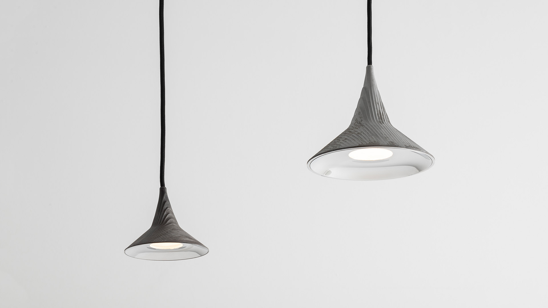 Due lampade da terra Artemide Unterlinden con stelo nero e base rotonda: sinistra con paralume argento, destra con paralume conico effetto legno