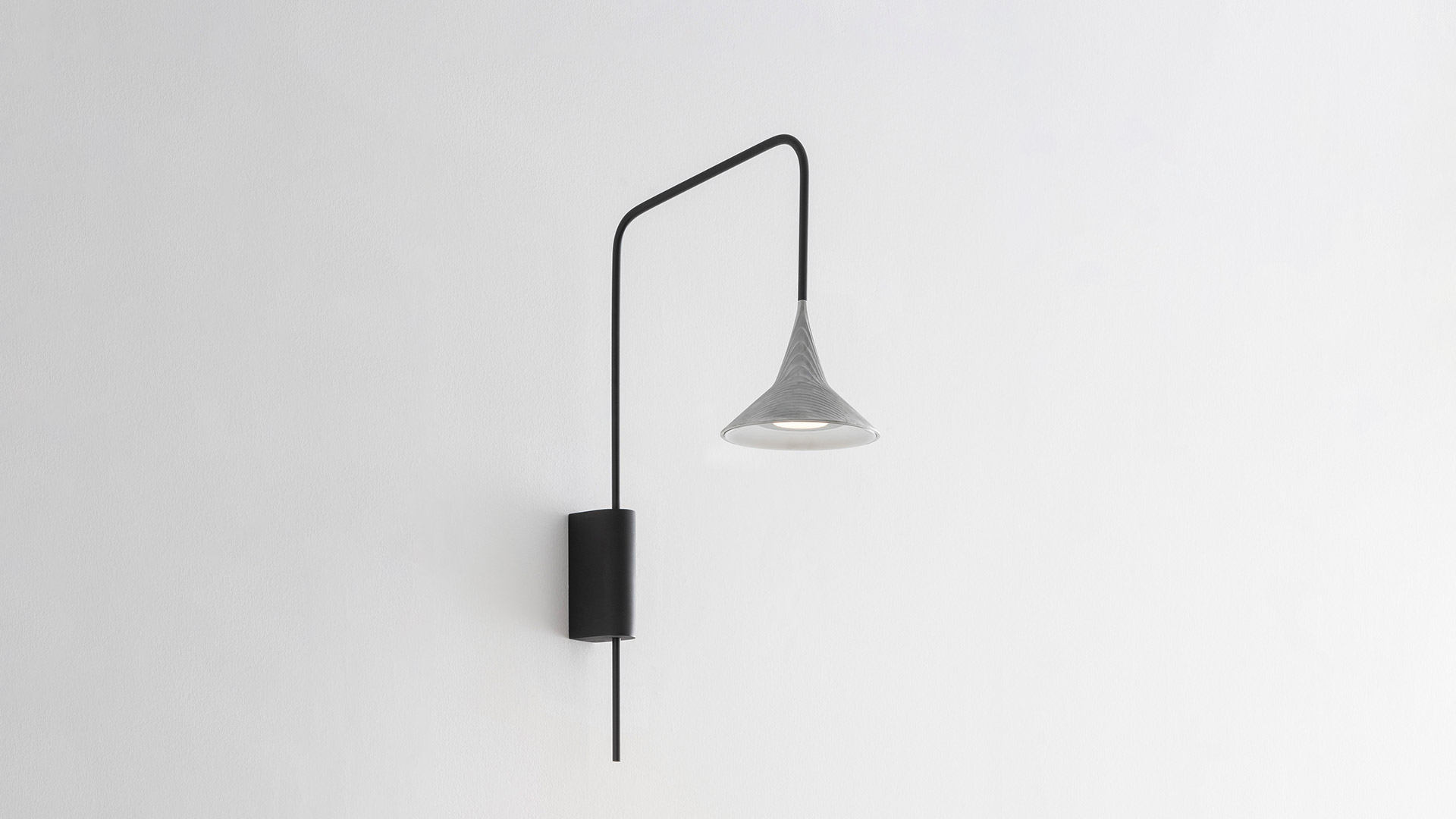Lampada da parete Artemide Unterlinden Outdoor: braccio in metallo nero che si estende dal supporto a parete, con paralume conico in alluminio appeso all'estremità