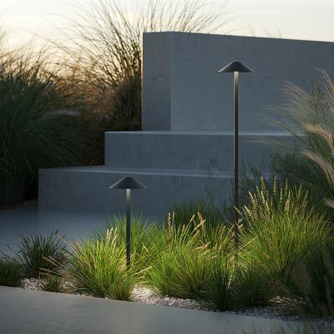 Due lampade da esterno Artemide Vea Bollard con paralumi conici scuri su pali sottili, che illuminano un giardino moderno al crepuscolo