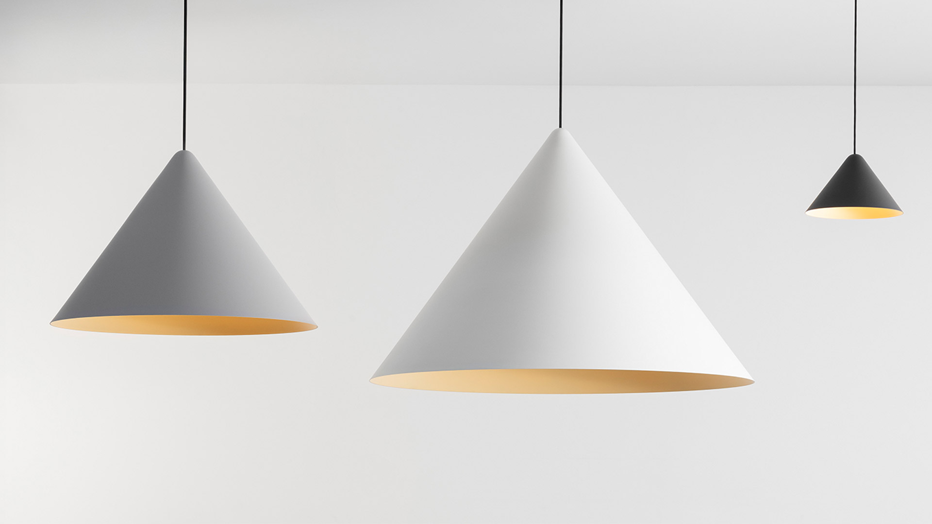 Tre lampade a sospensione Artemide Vea con paralumi conici in grigio, bianco e nero e interno dorato caldo, appese a cavi neri