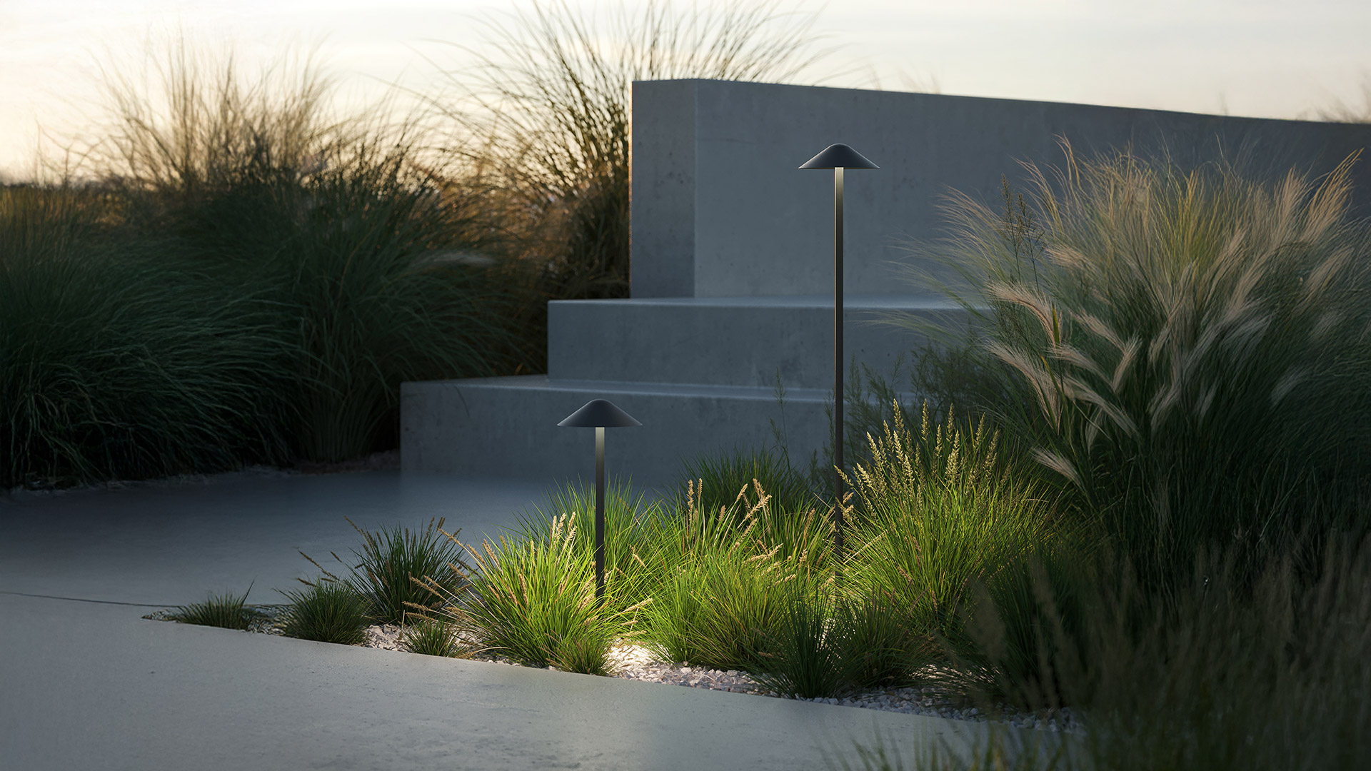 Due lampade da esterno Artemide Vea Bollard con paralumi conici scuri illuminano erbe ornamentali in un giardino minimalista al crepuscolo