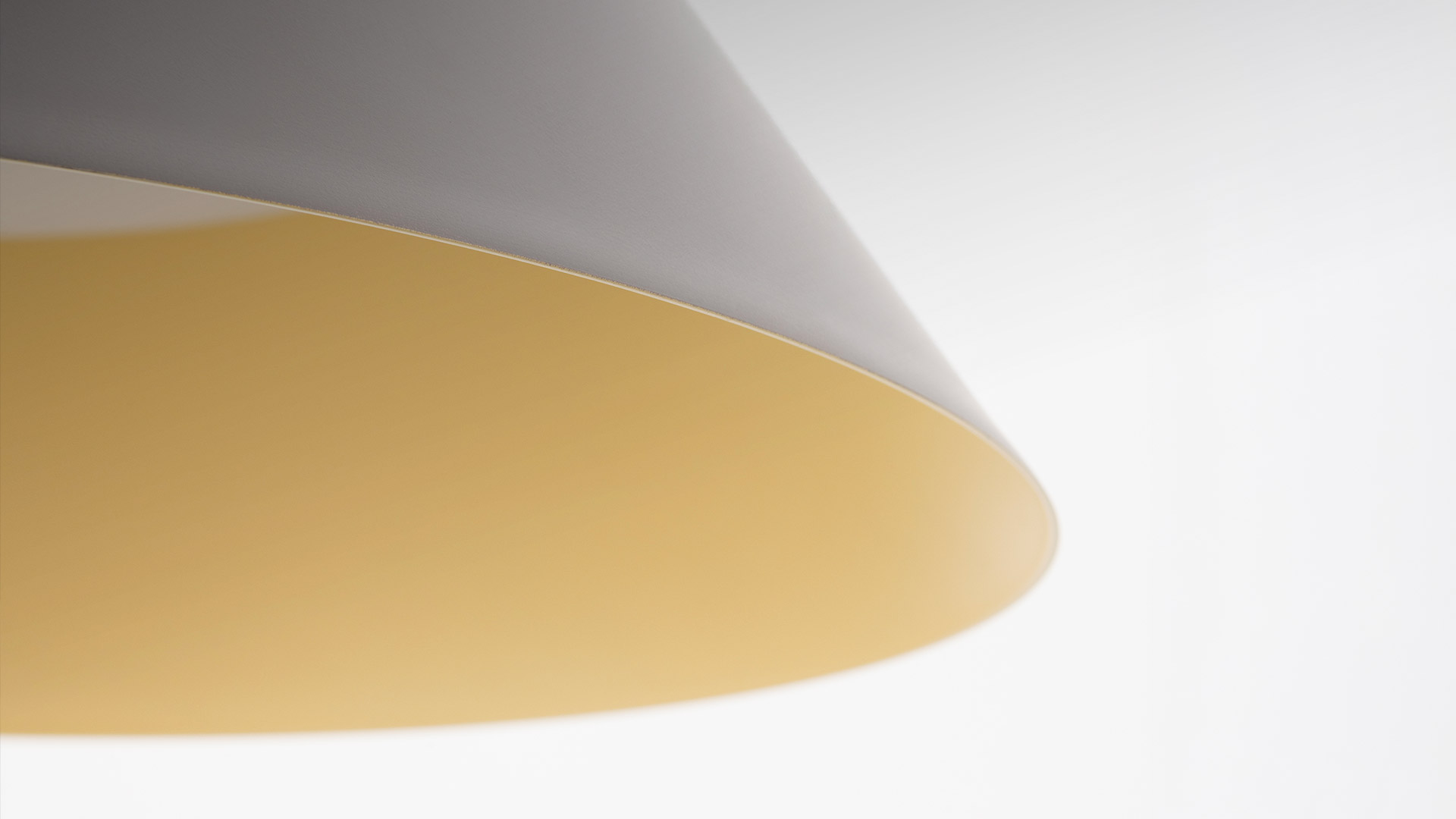 Lampada a sospensione Vea di Artemide: paralume conico grigio scuro con interno dorato caldo, sospesa sopra oggetti decorativi scultorei bianchi su una superficie