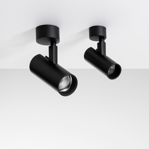 Two Artemide Vector Ceiling black spotlights mounted on ceiling, cylindrical heads adjustable on articulated arms, one showing LED lens