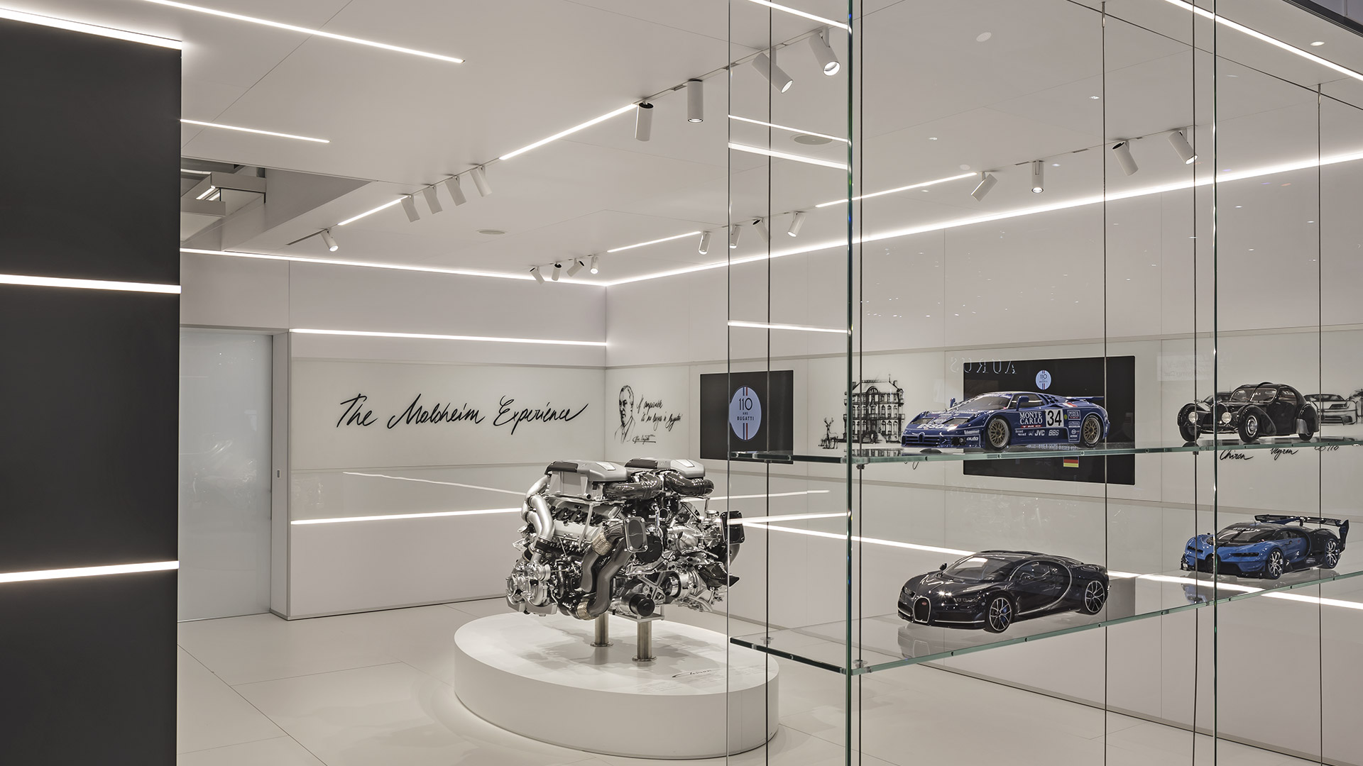 Luci lineari LED Artemide Vector e Vector Magnetic illuminano un elegante showroom automotive con motore Bugatti e modelli in scala